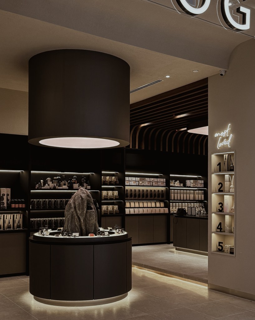 Interior view of HOOGA store featuring a central sculptural stone centerpiece and dark wood shelves displaying various homeware products, illuminated with soft lighting.