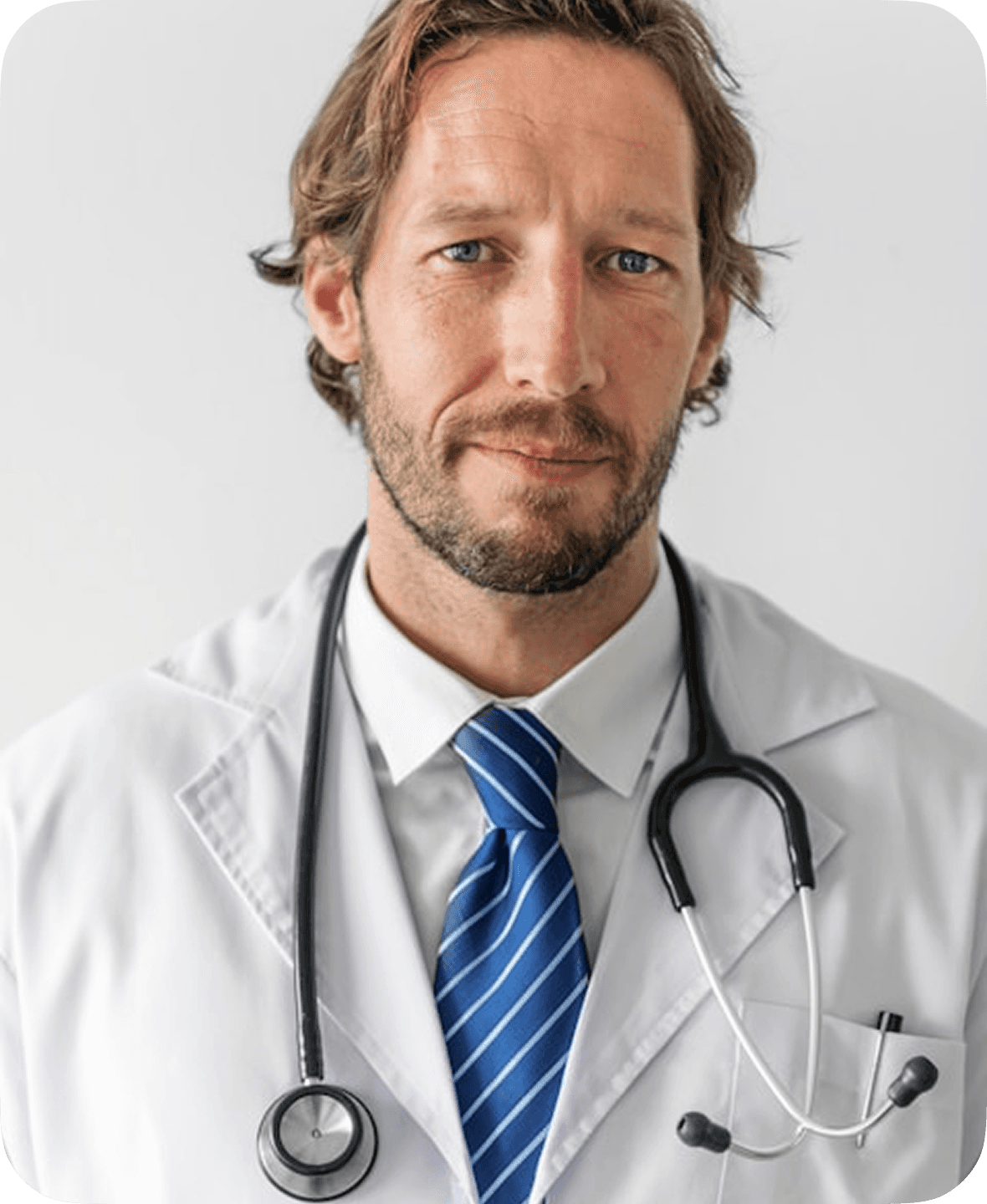 A male doctor with a neatly groomed beard is wearing a white lab coat and a stethoscope around his neck, standing against a plain white background.
