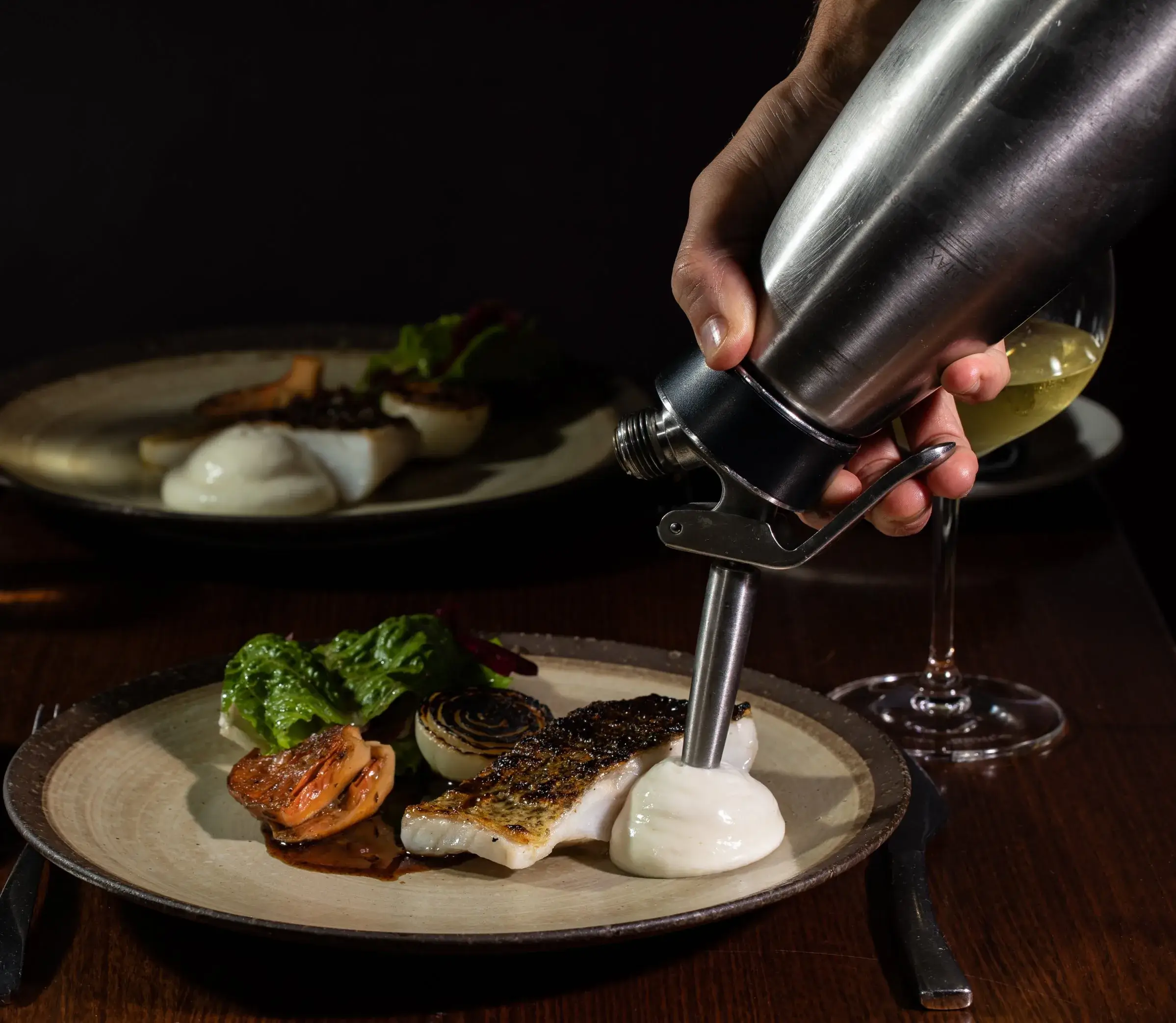 Chef finishing a crisp-skin barramundi dish with sauce at ANNATA