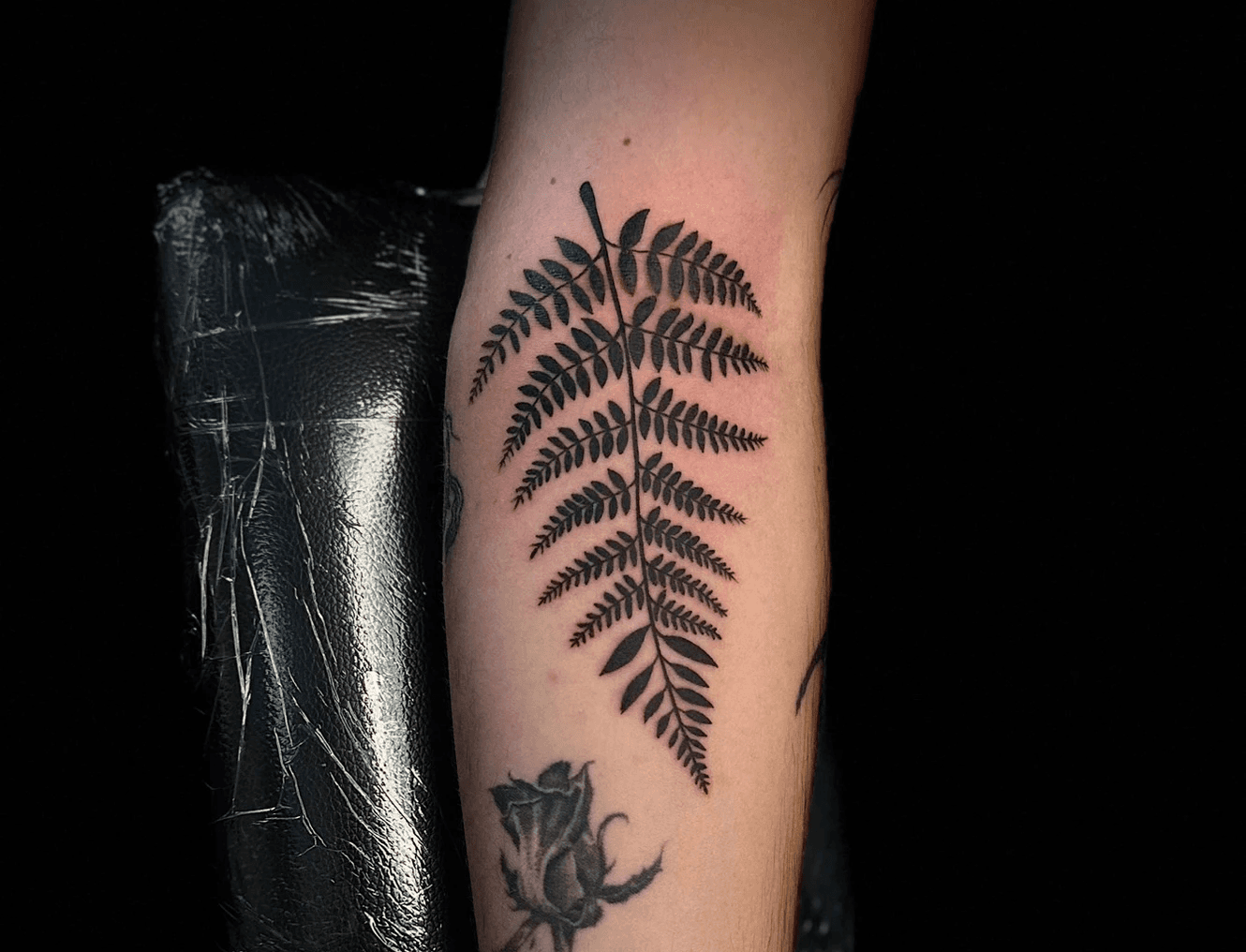 Finely detailed tattoo of a snake intertwined with delicate floral motifs on the wrist and hand area. Inked by Jai at Bloodworks Tattoo Studio, Auckland.