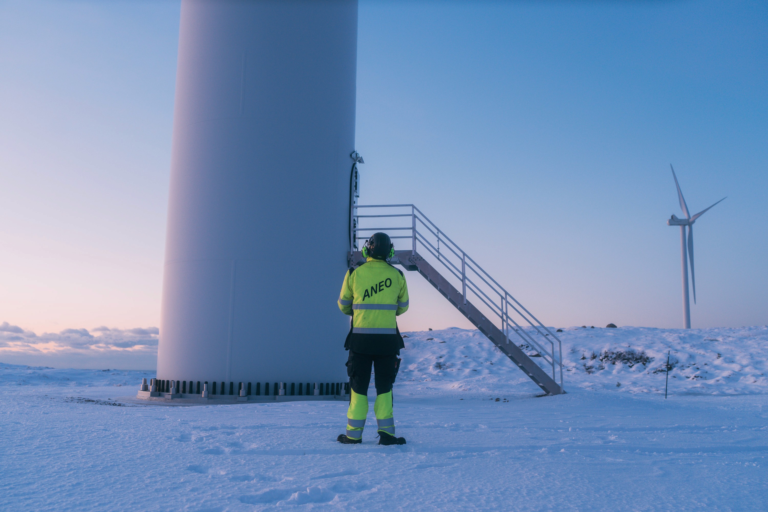 Vindkrafttekniker står i vinterkulda og ser opp på en vindturbin