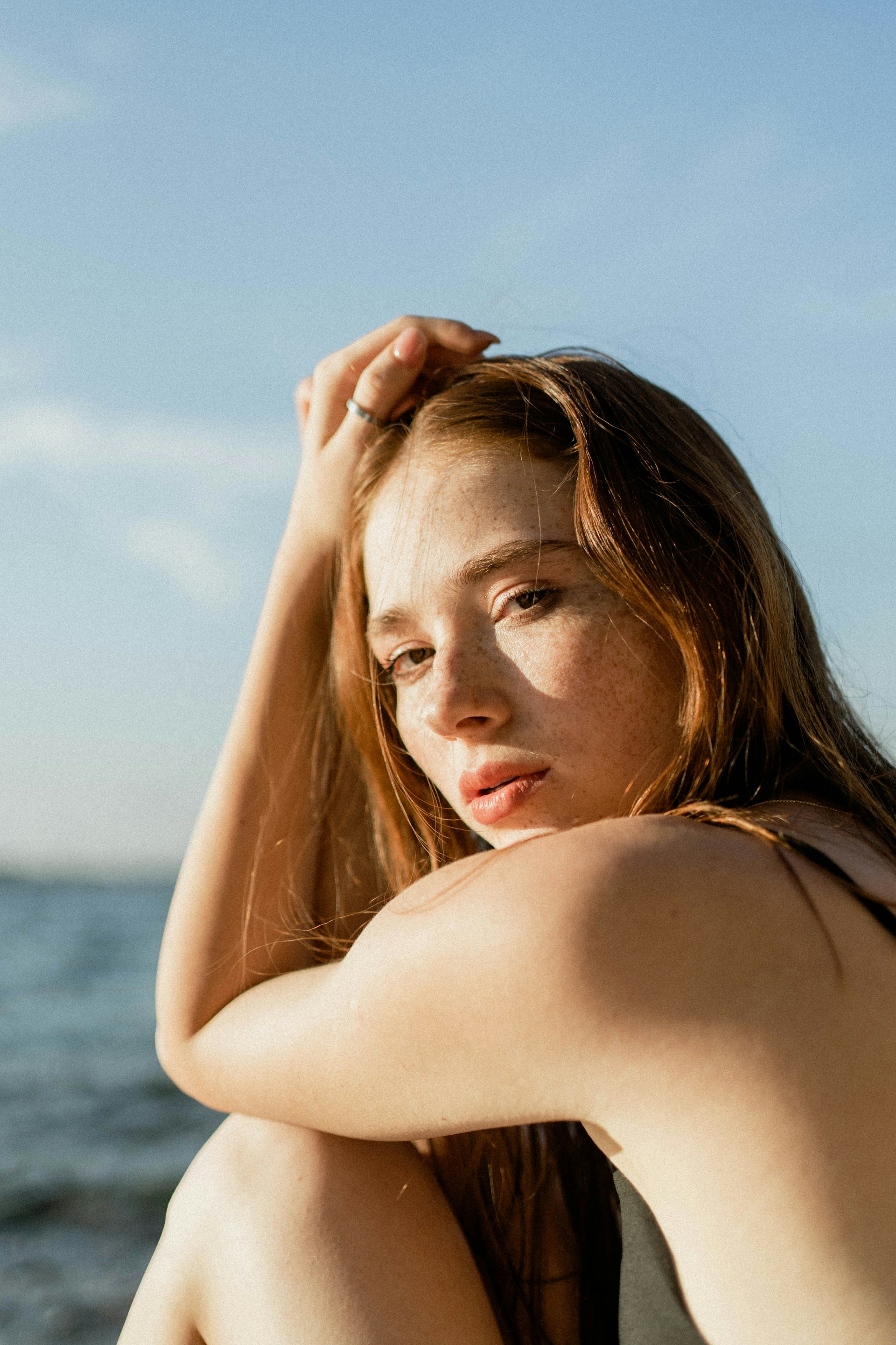 Portrait of a red-haired woman with freckles posing by the sea.