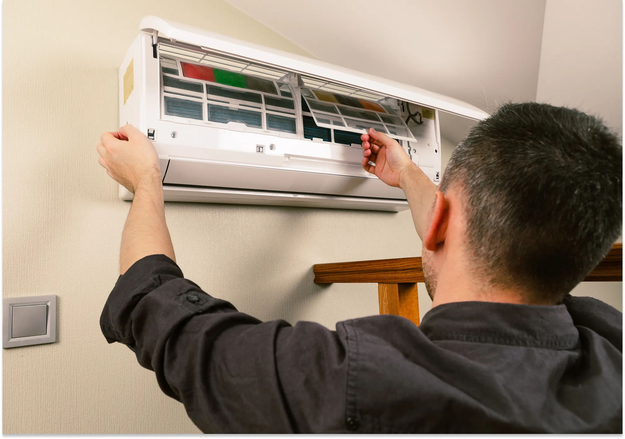 Homeowner or technician adjusting the air filter or front panel of a wall-mounted indoor air conditioning unit.