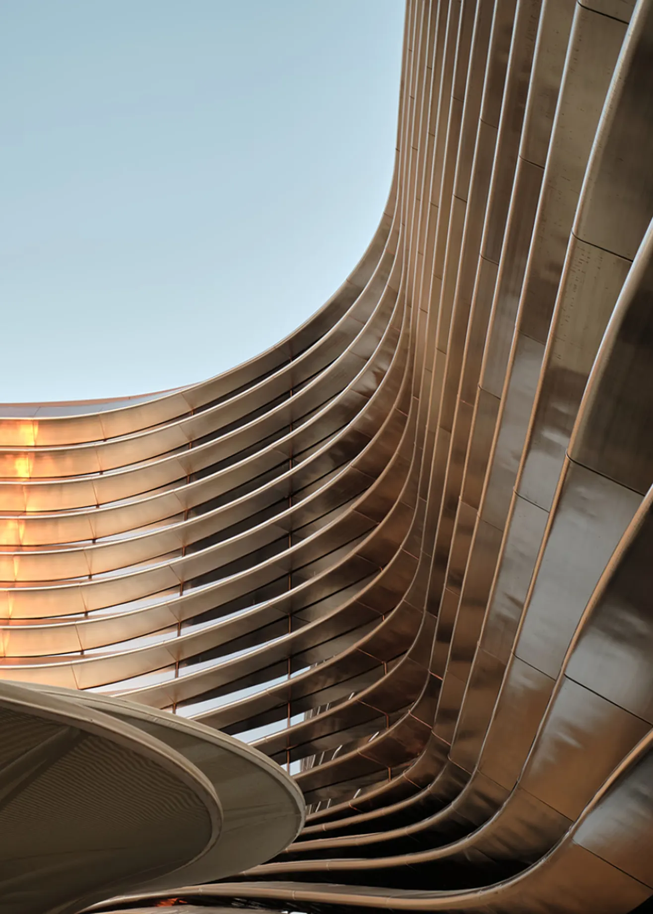 Abstract curved building exterior with rhythmic wooden fins or slats under a bright sky.
