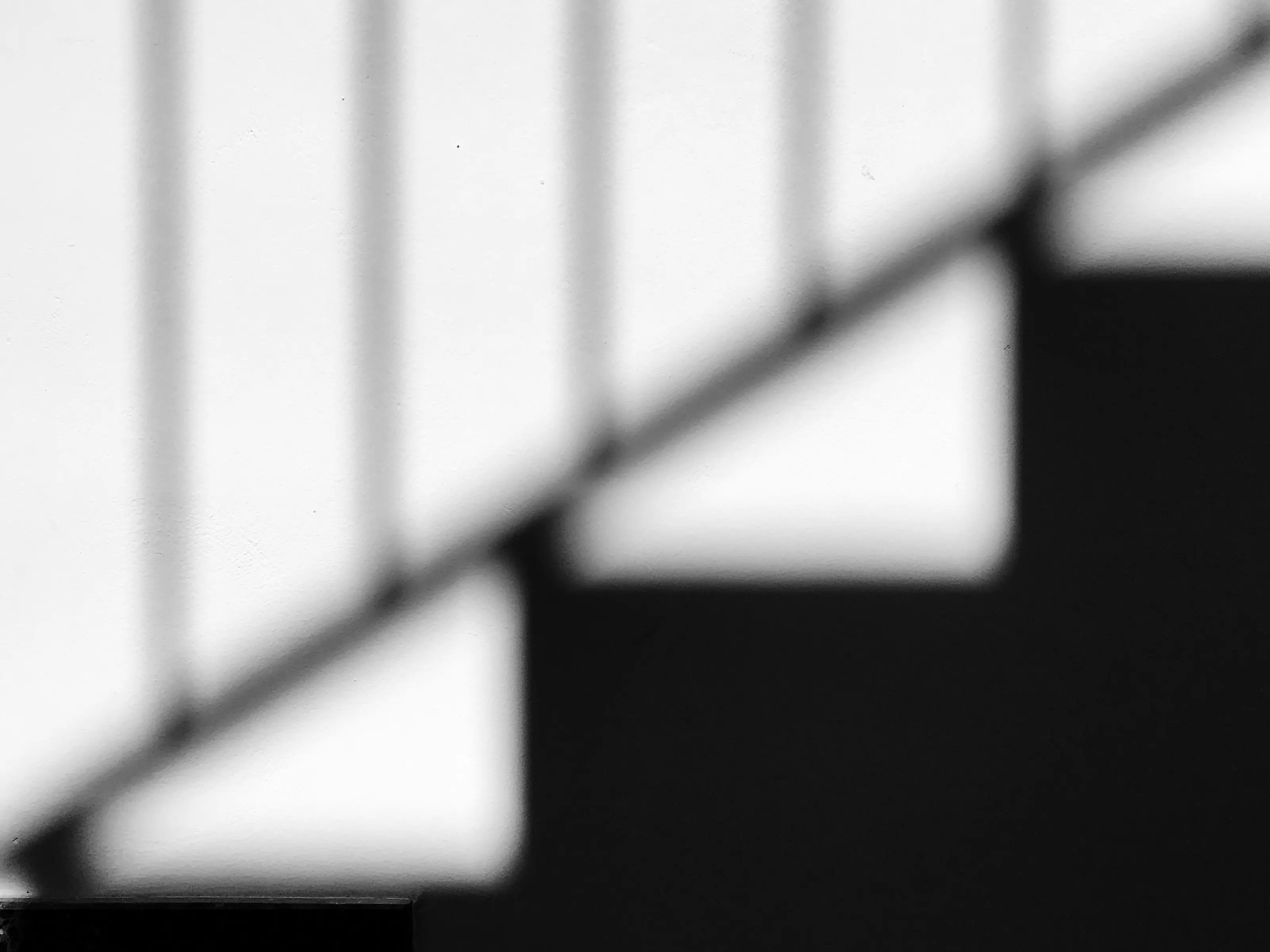 Blurred black and white photograph of a staircase railing's shadow cast diagonally across concrete steps