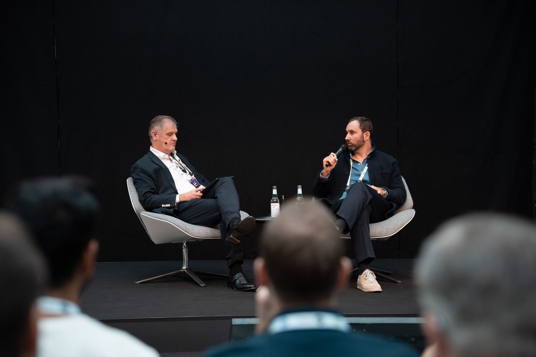 Two colleagues talking across a table with a laptop and coffee cup