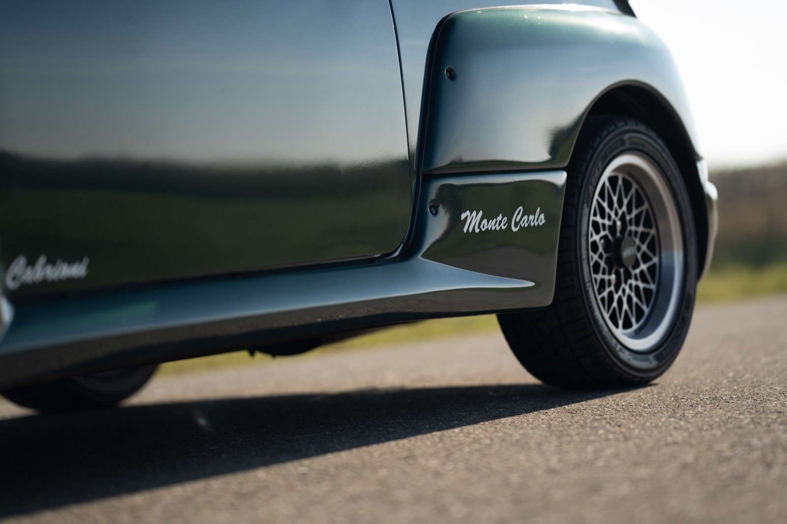 Close-up of a sleek car's side, showcasing the lower body and wheel with a blurred background.