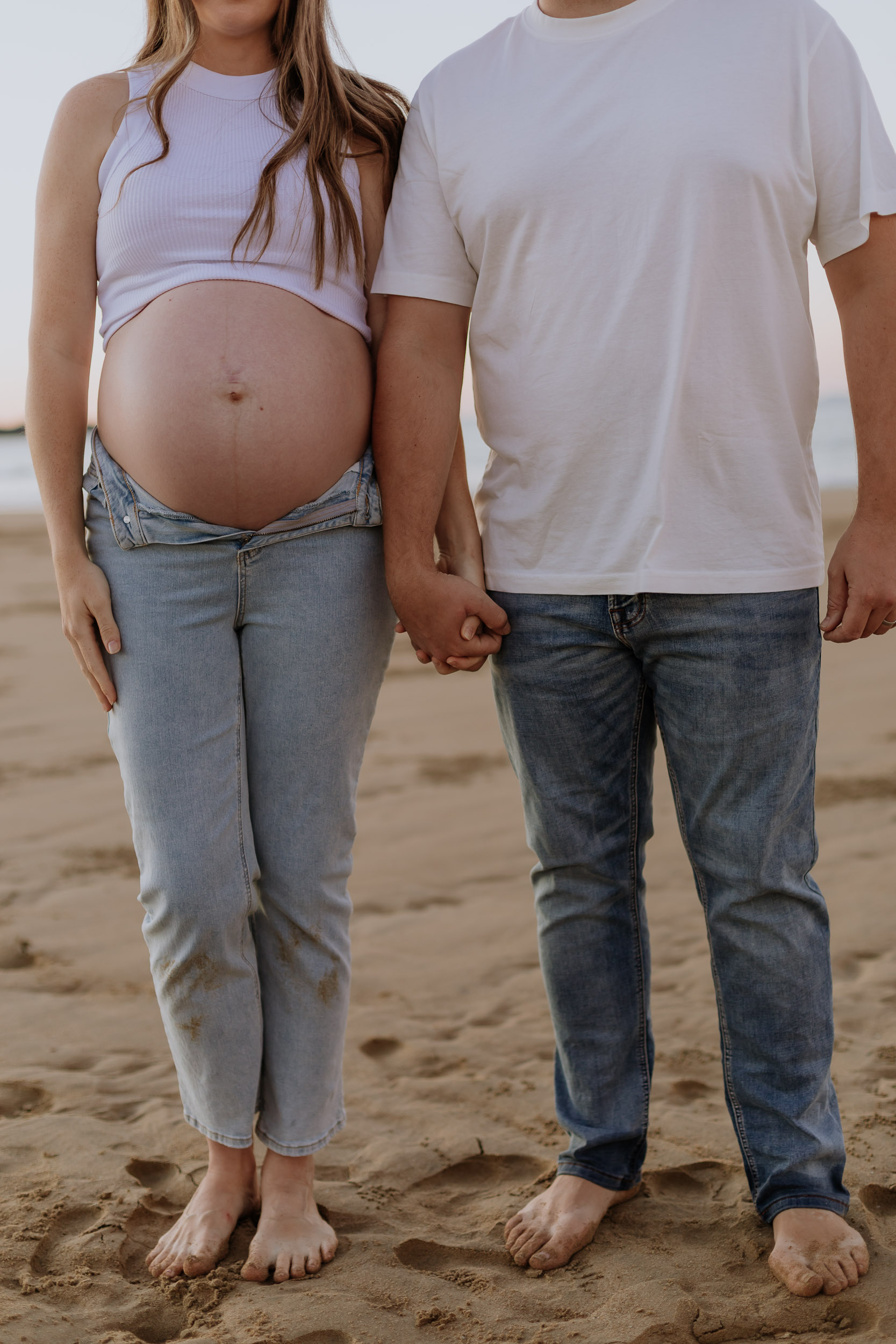 Pregnant couple holding hands on the beach in Mackay