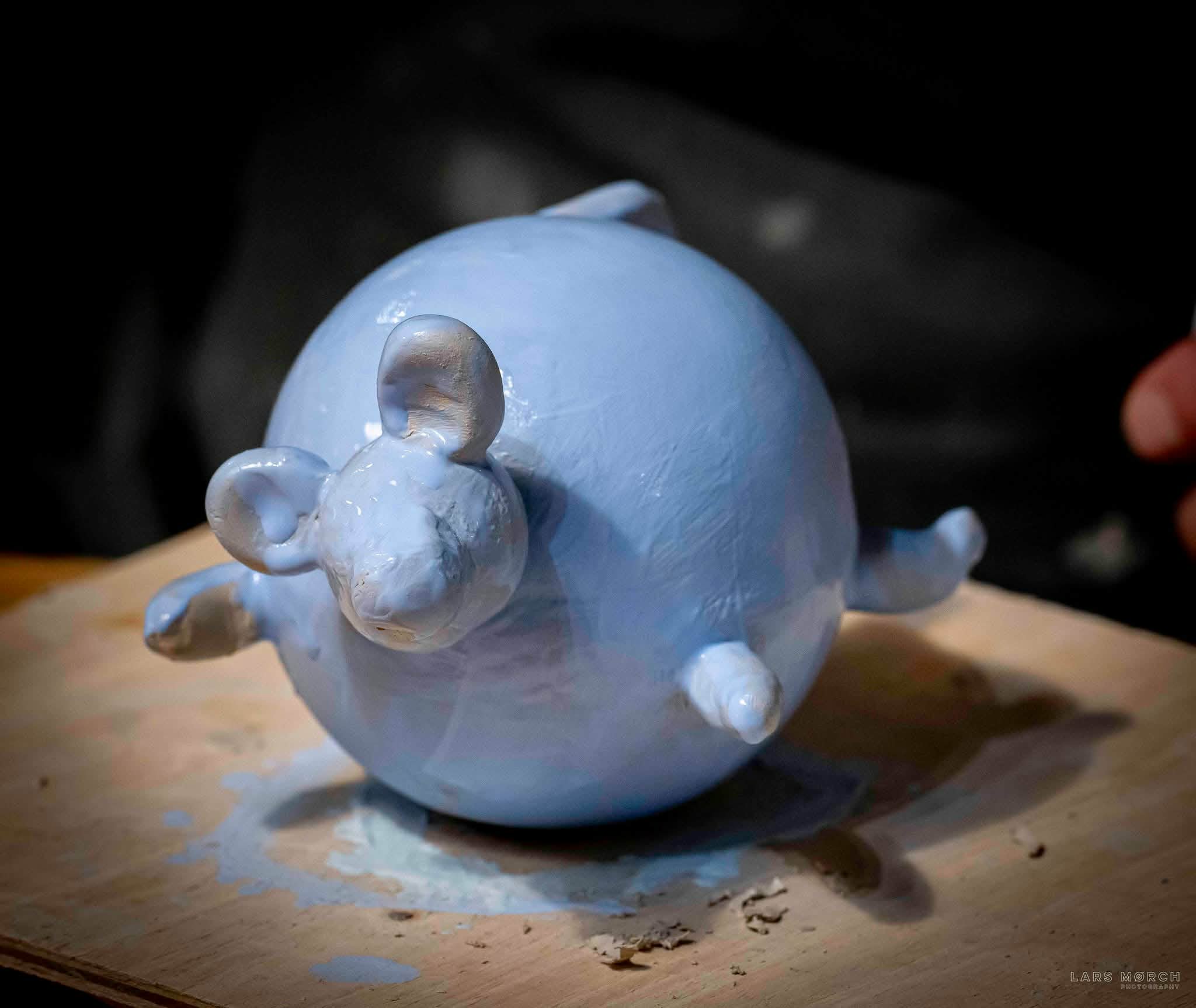 a funny piece of greenware shaped like a round mouse painted with light blue underglaze