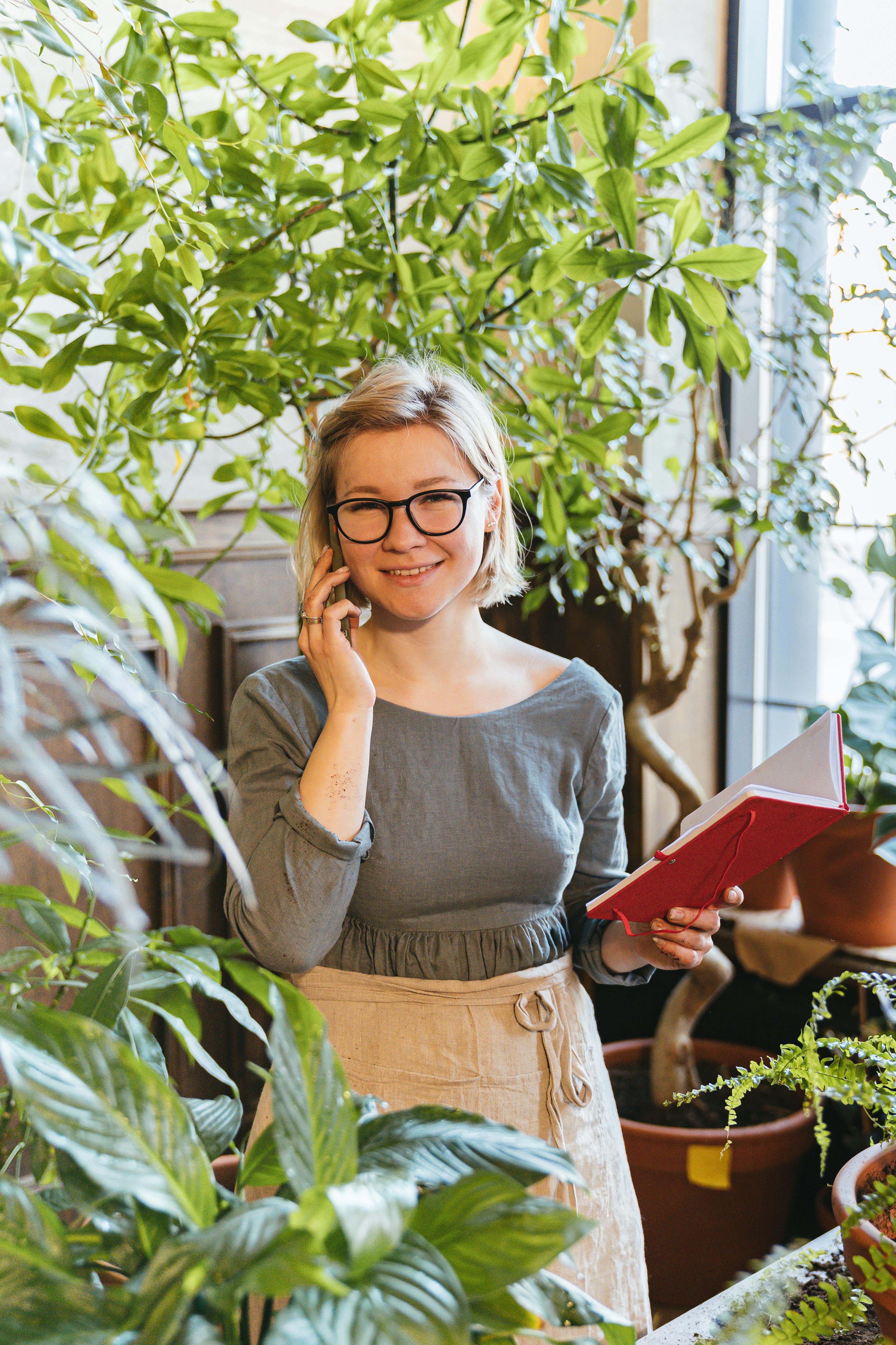 smiling-woman-gardener-in-apron-using-phone-and-notebook-among-indoor-plants. - antoni-shkraba-studio (pexels)