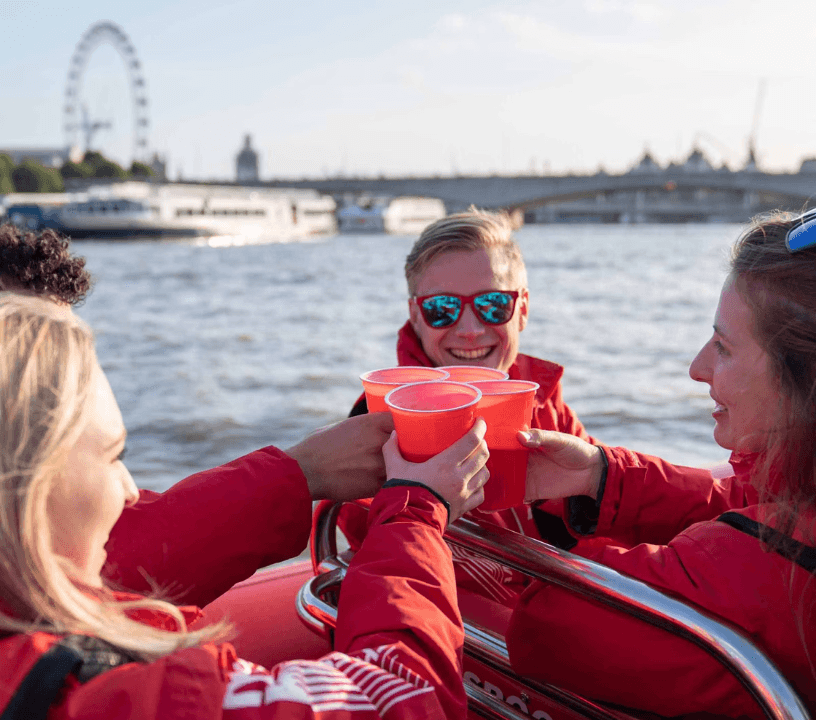 Thames Rockets Nights Speedboat Experience: A group of three friends face each other and toast with the London Eye in the background