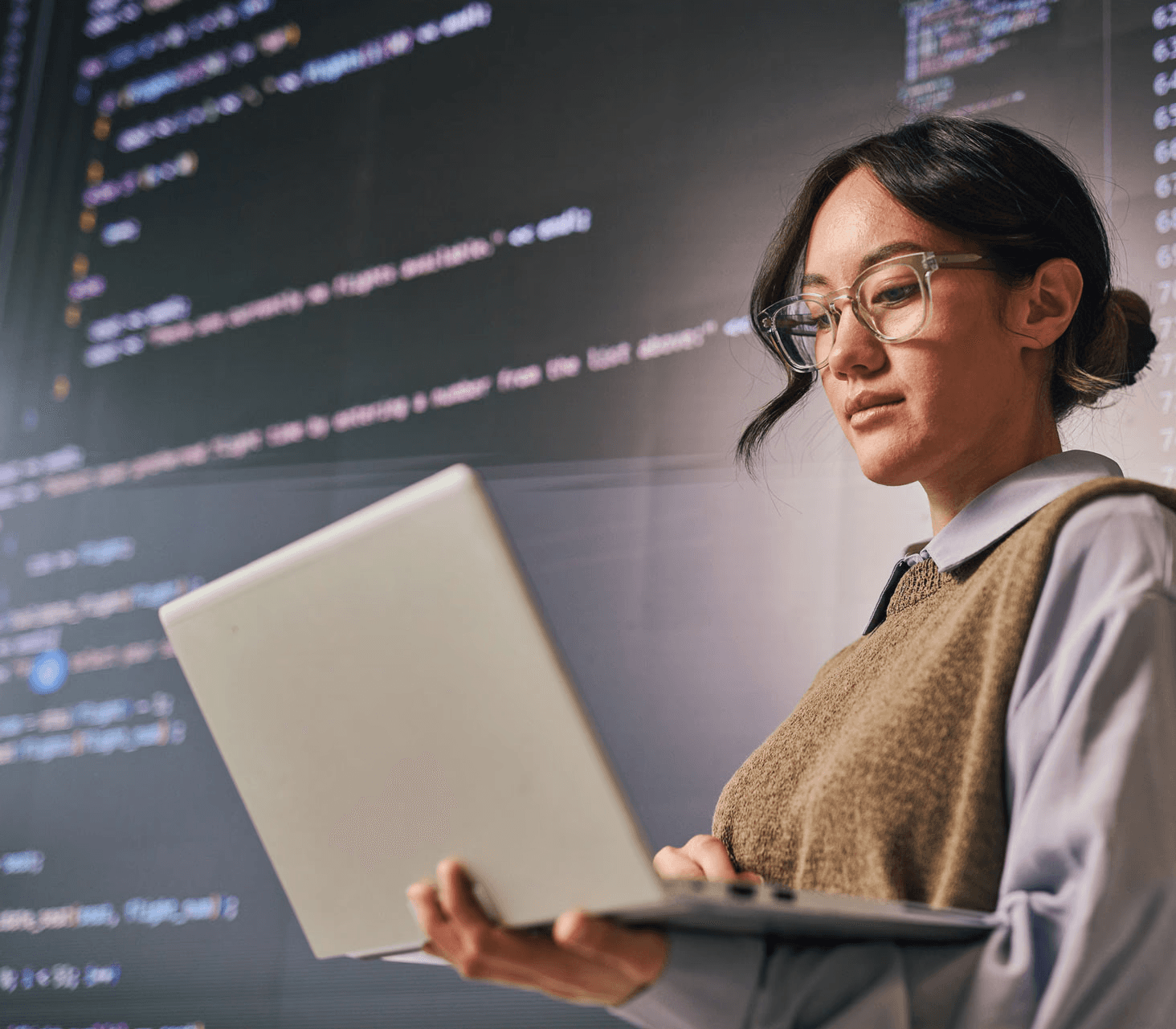 Young programmer analyzing code on laptop and large screen in modern office