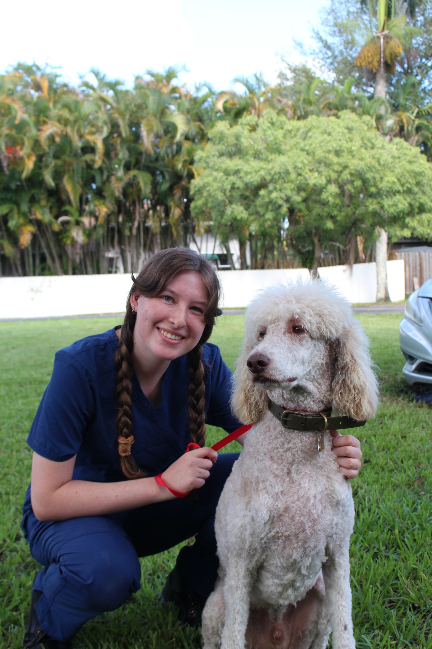 zoe kneeling on the grass with a standard poodle