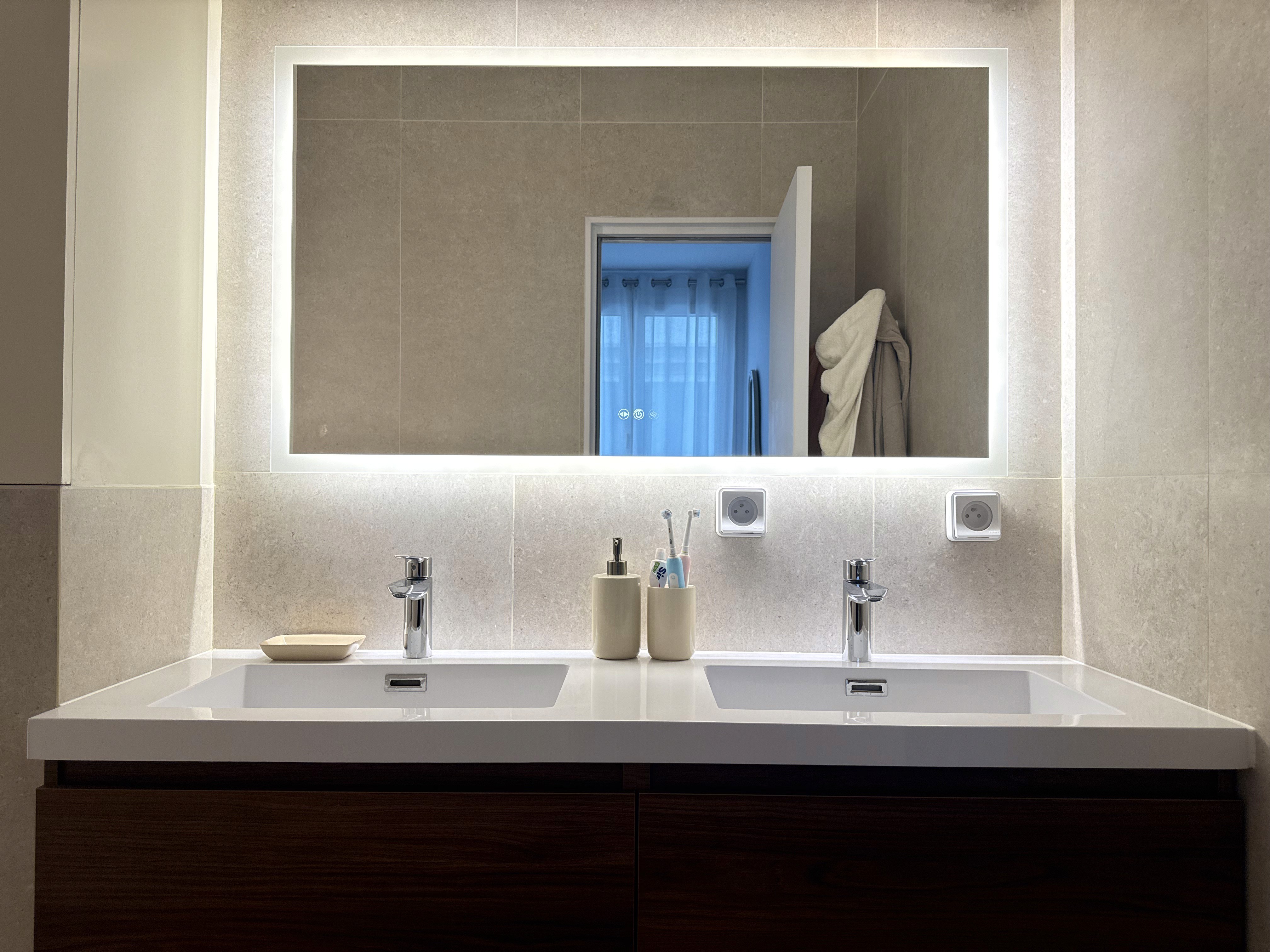 Salle de bain contemporaine avec double vasque, grand miroir rétro-éclairé par LED et meubles de rangement en bois sombre.