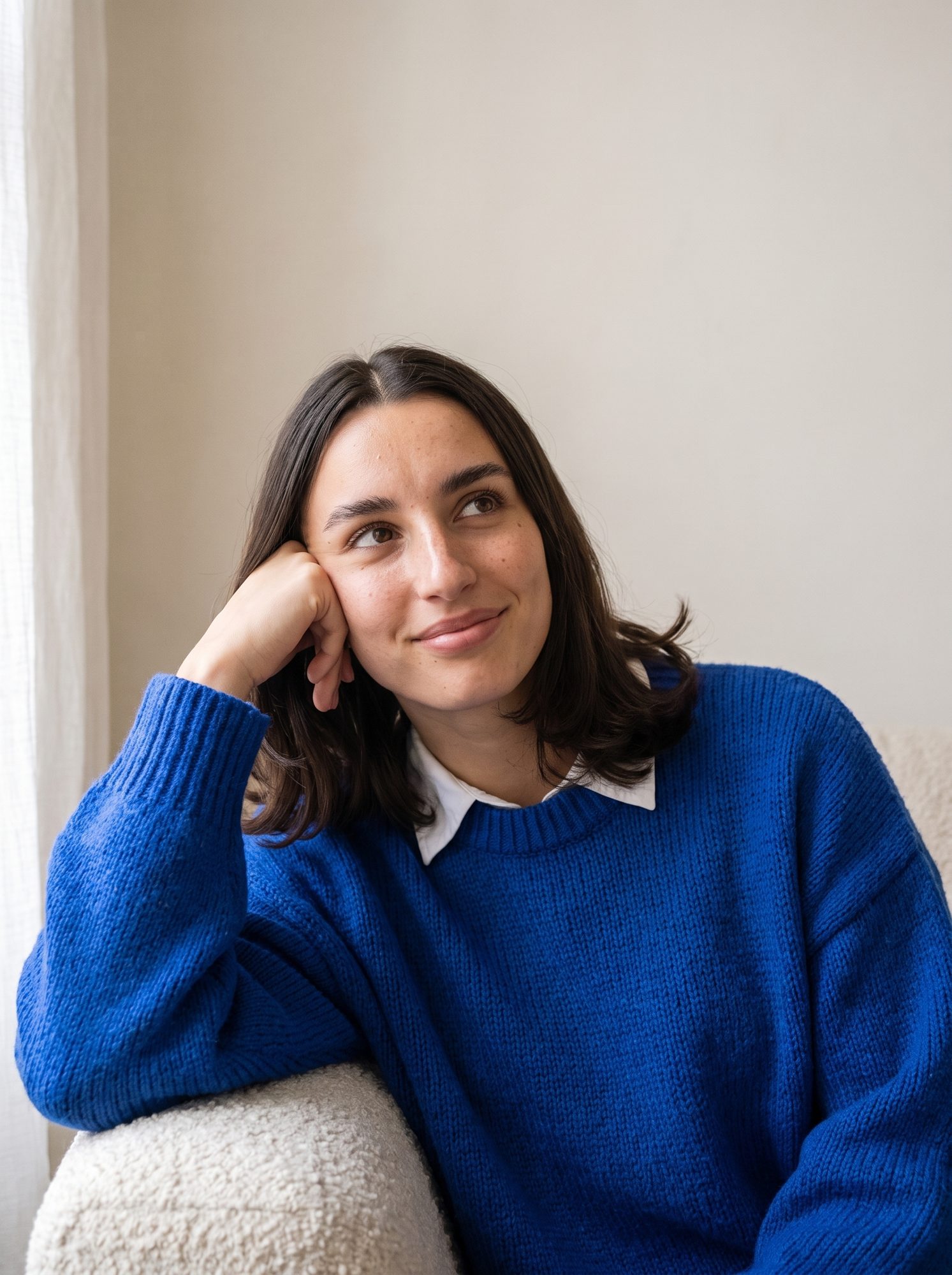 Portrait of Grace Ellery leaning on the arm of a sofa, resting her head on her hand and smiling.