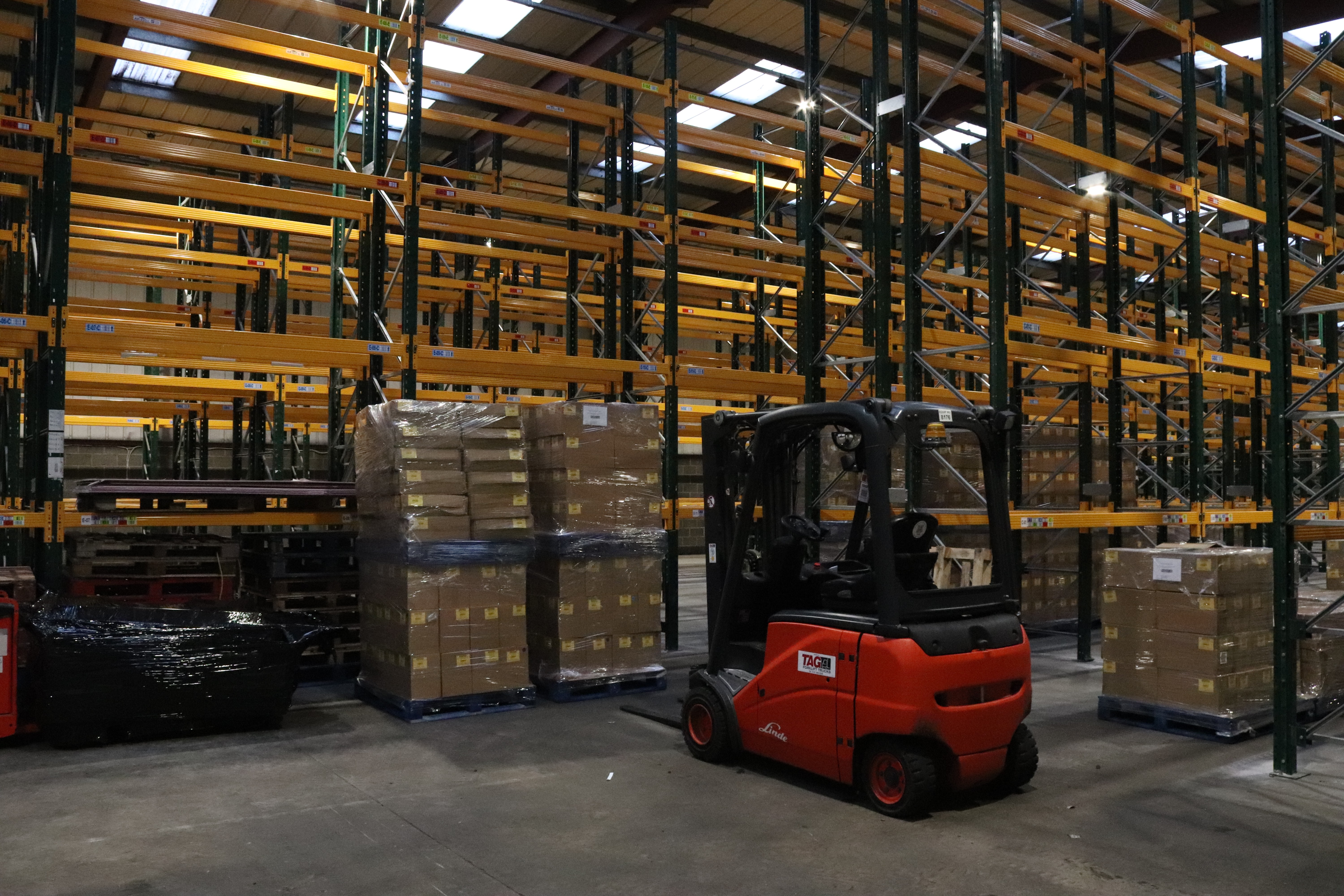 image of a warehouse with racking a forklift and pallets all waiting to be moved