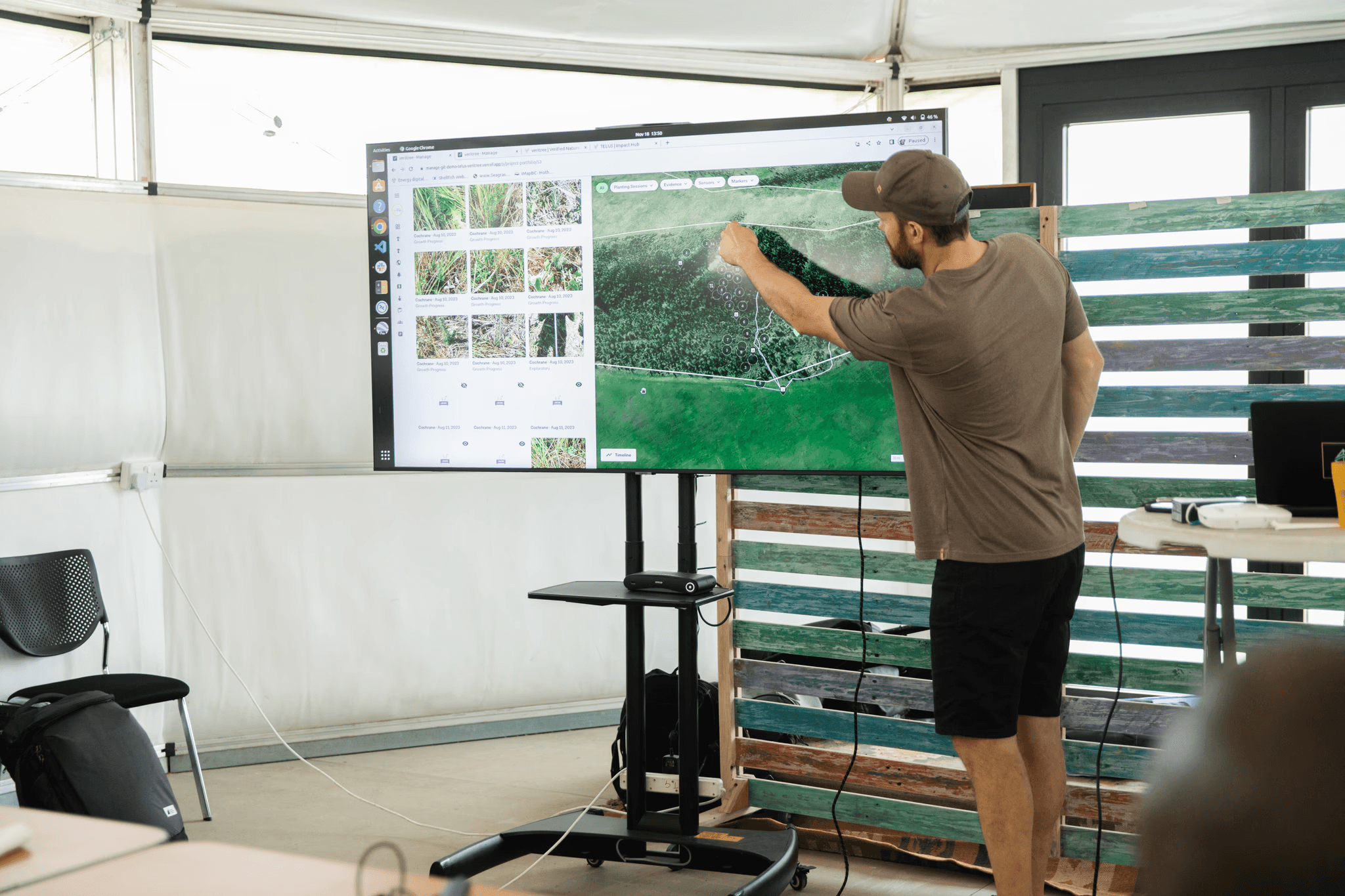 Man die wijst naar een groot scherm met digitale kaarten en voortgangsgrafieken van inspanningen voor boomaanplant, met de nadruk op real-time tracking met veritree.