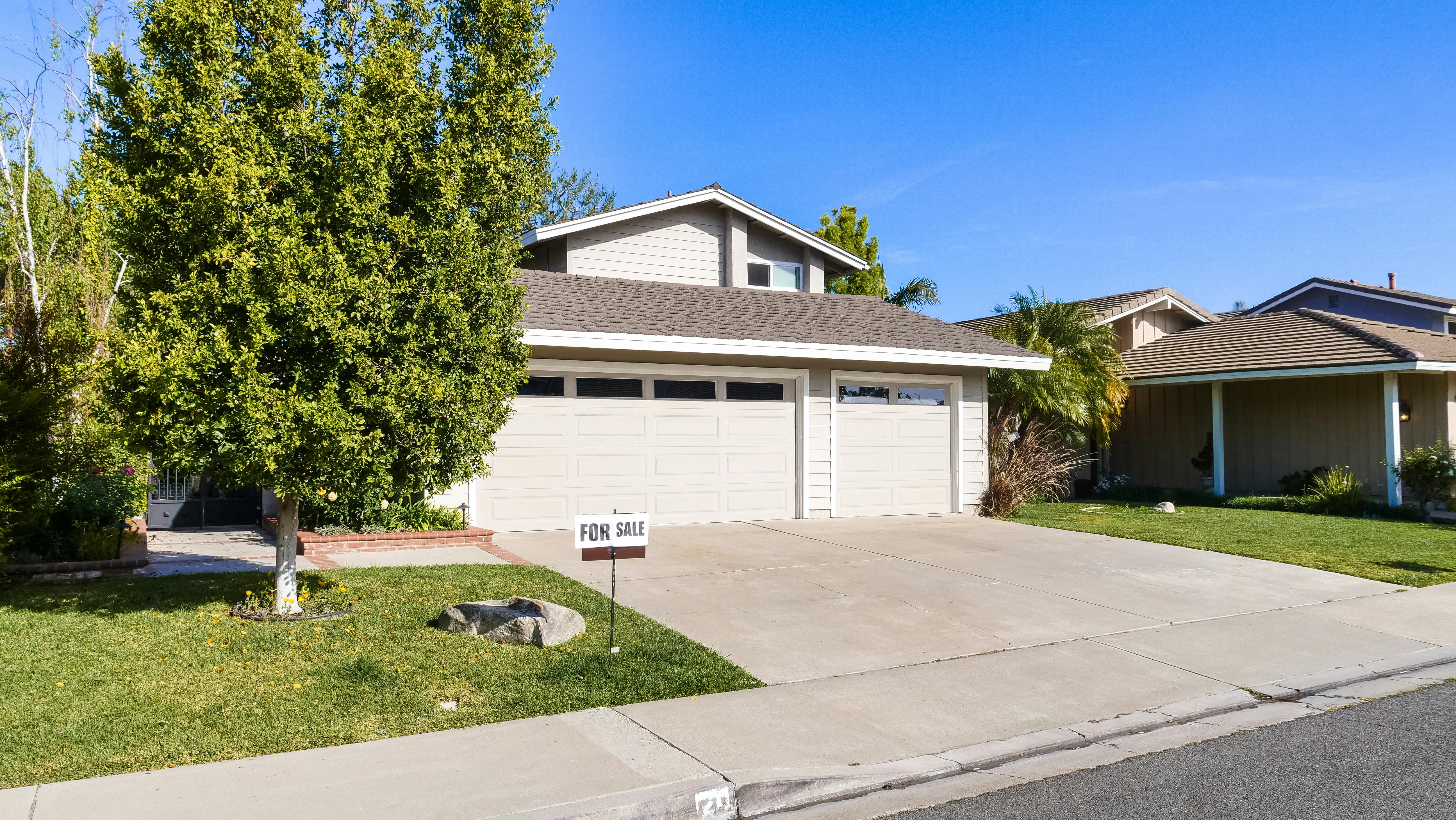 A suburban house with a two-car garage, green lawn, and trees under a clear blue sky.