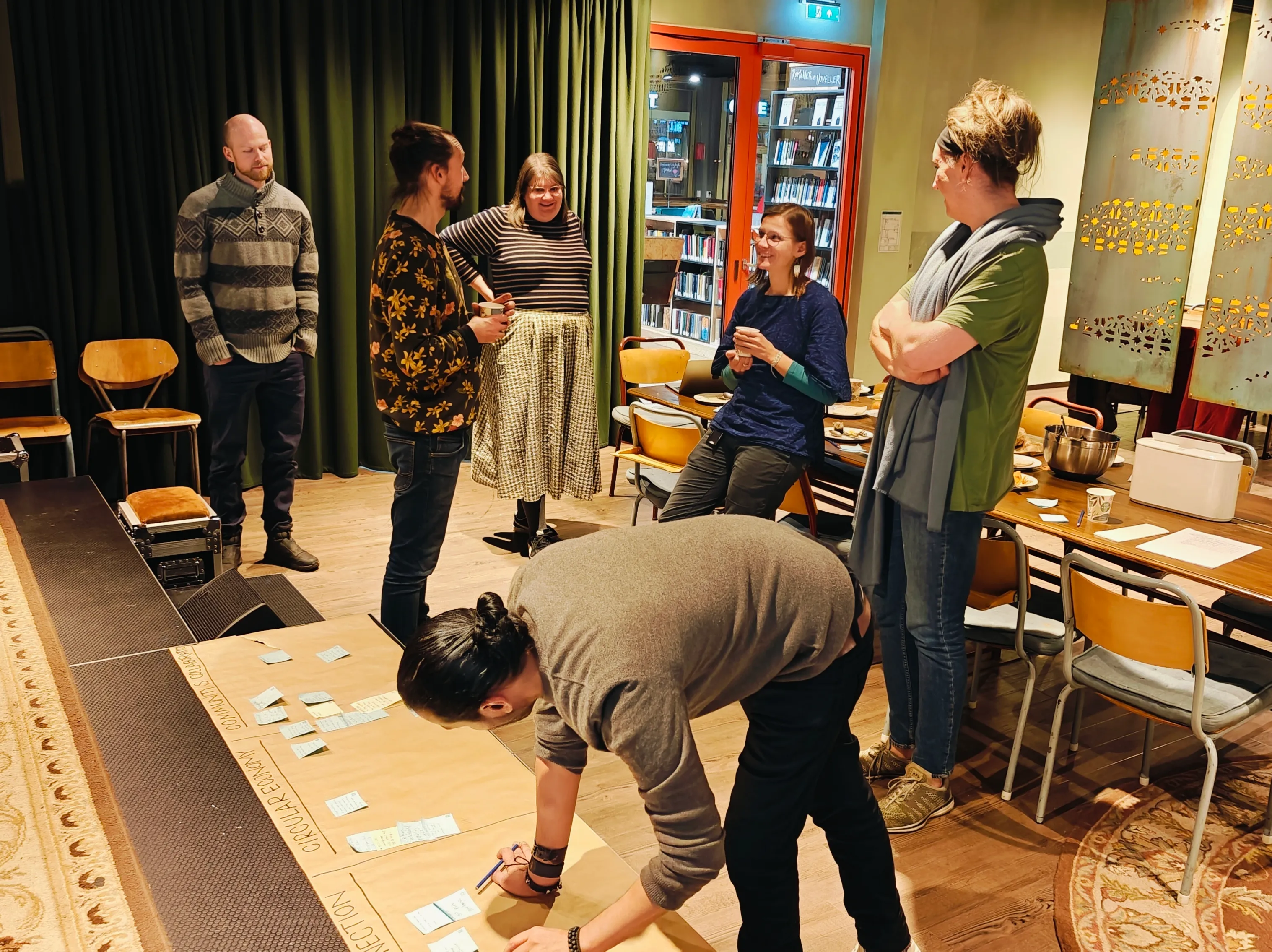 People talking in a room and one person putting down sticky notes on a board