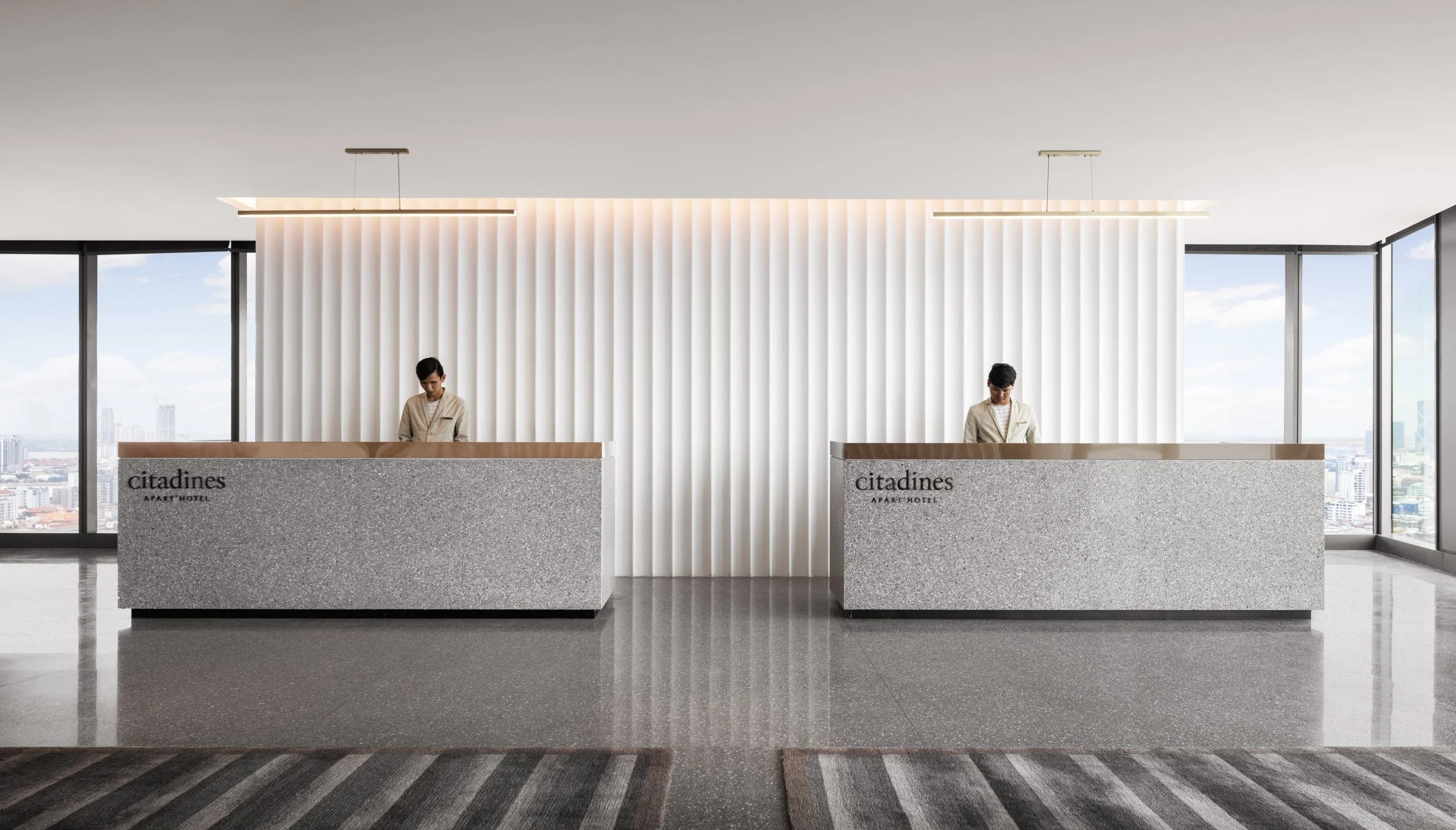 Dual monolithic stone reception counters, architectural fluted wall treatment, panoramic urban skyline views.