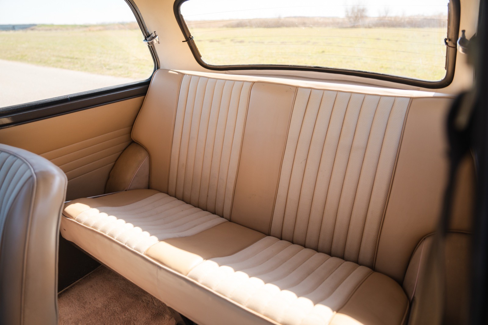 Interior view of a vintage vehicle's back seat, featuring beige fabric upholstery and a scenic view outside.