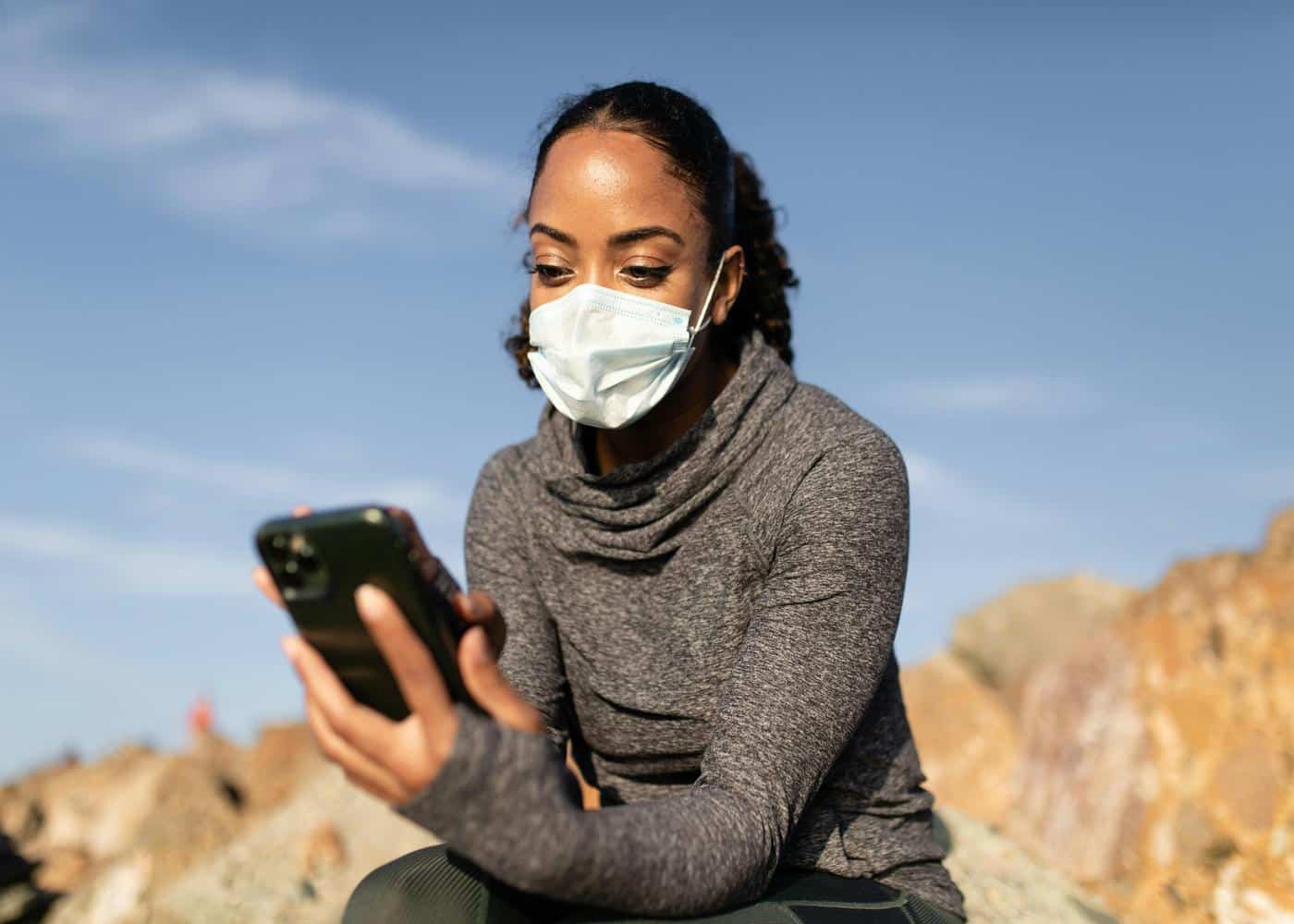 Woman outdoors with facemask on looking at smart phone