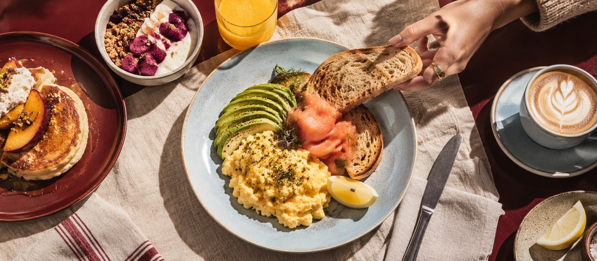 Friends passing plates of scrambled eggs, salmon and pancakes across the long table at MORNI