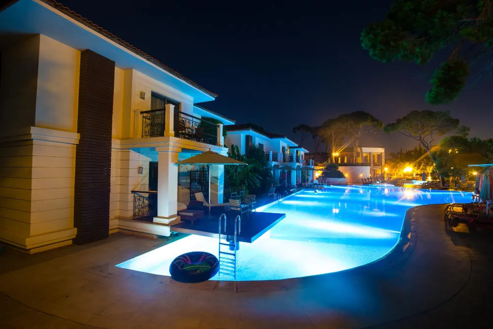 Nighttime view of a resort-style pool illuminated by underwater and landscape lighting.
