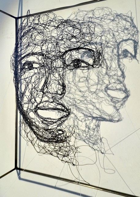 Sculpture en fil de fer représentant le visage d'une femme dans un cadre en fil de fer, vue détaillée de profil avec son ombre projetée sur le mur