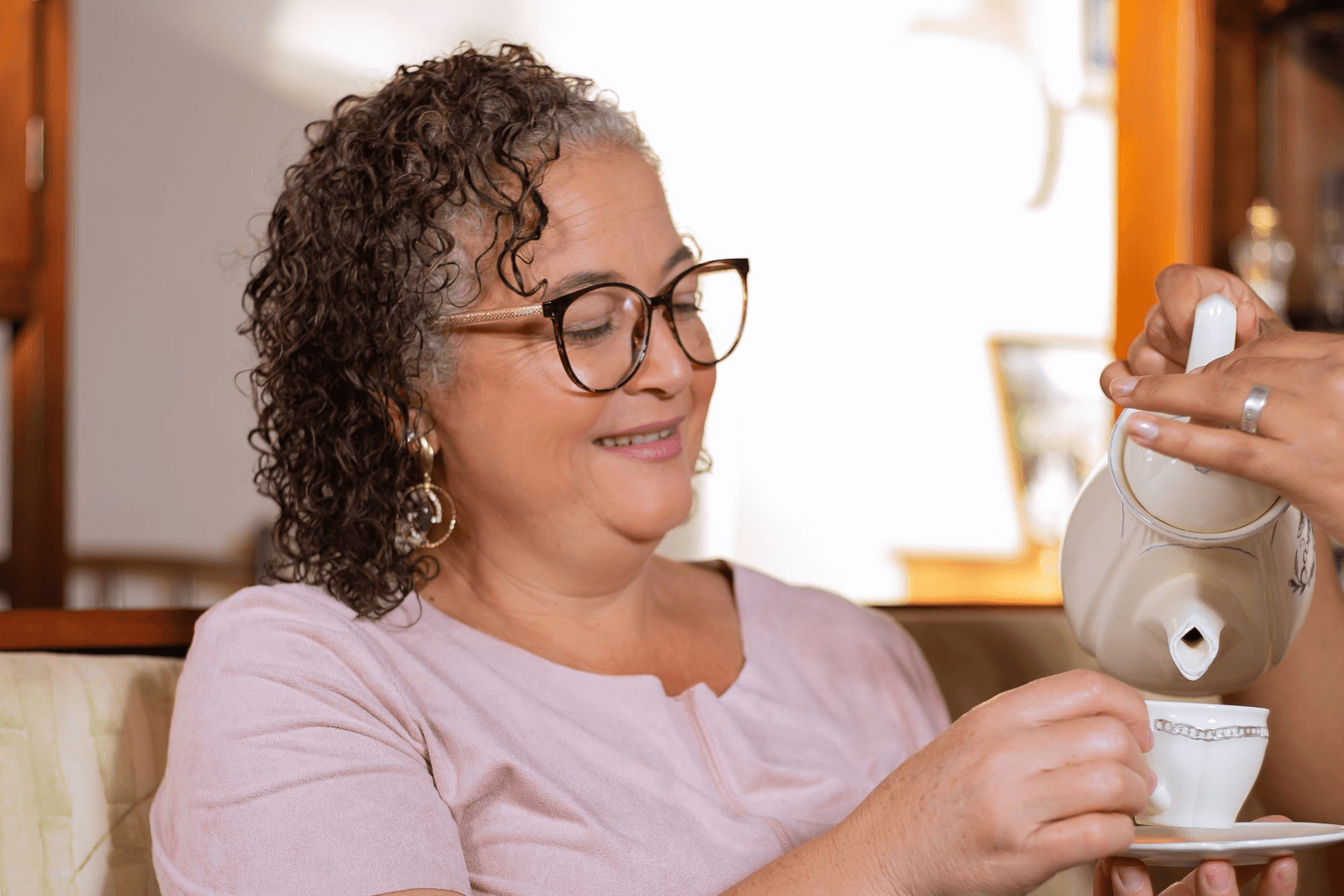 A woman pouring herself a cup of tea at home, taking a moment to sit down.