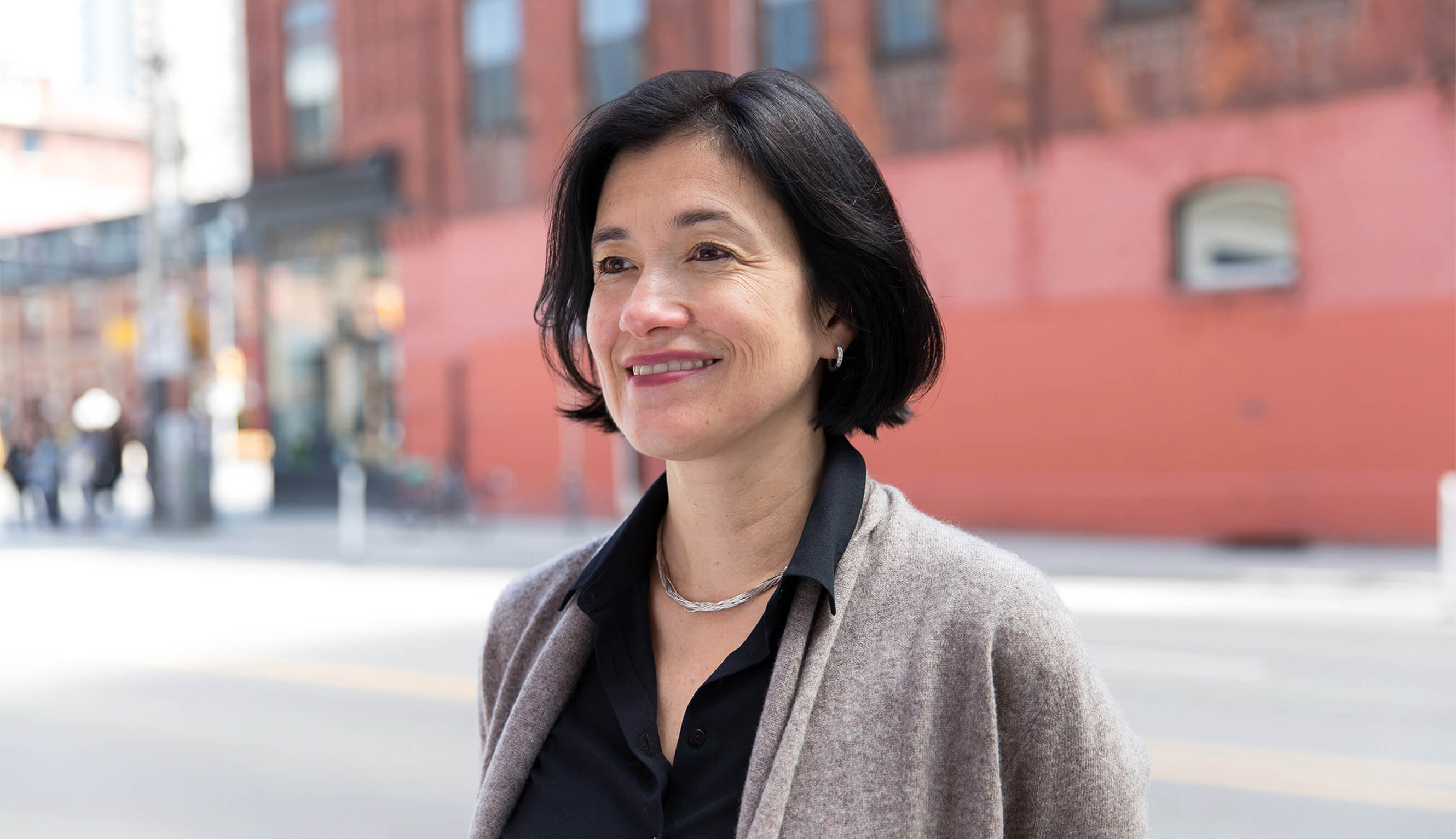 Headshot of a similing professional woman in front of a red building.