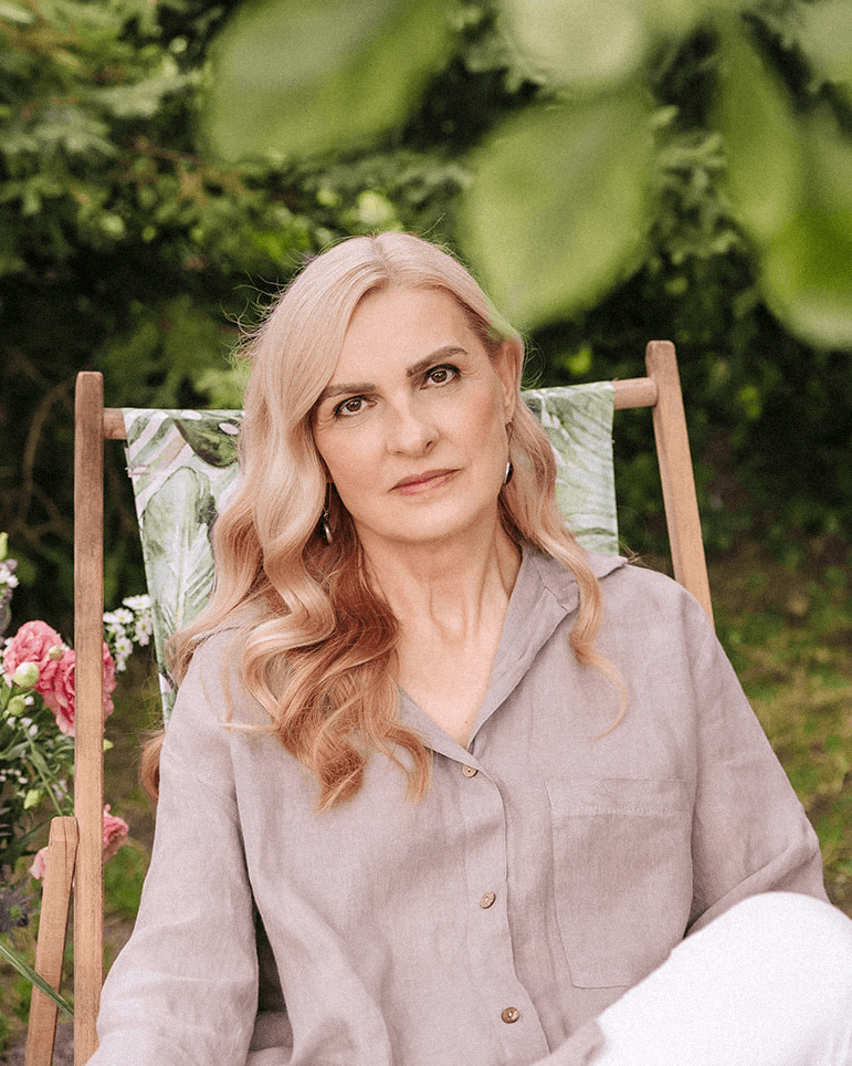 Beata Grala, psychoterapeutka, autorka warsztatów siedzi na krześle w ogrodzie.