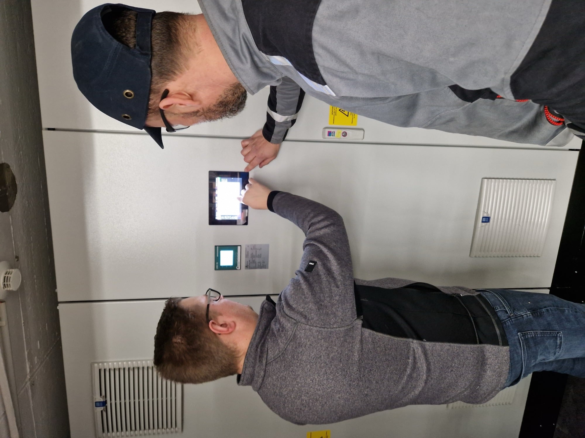 Zwei Fachleute stellen Einstellungen am digitalen Bedienfeld in einer industriellen Arbeitsumgebung ein.