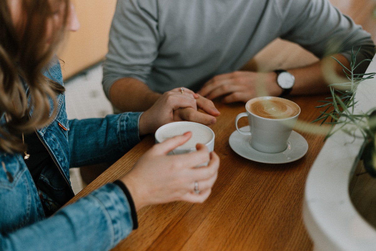 Two people sitting close over coffee, one offering a supportive hand, representing walking through recovery alongside a caring dietitian