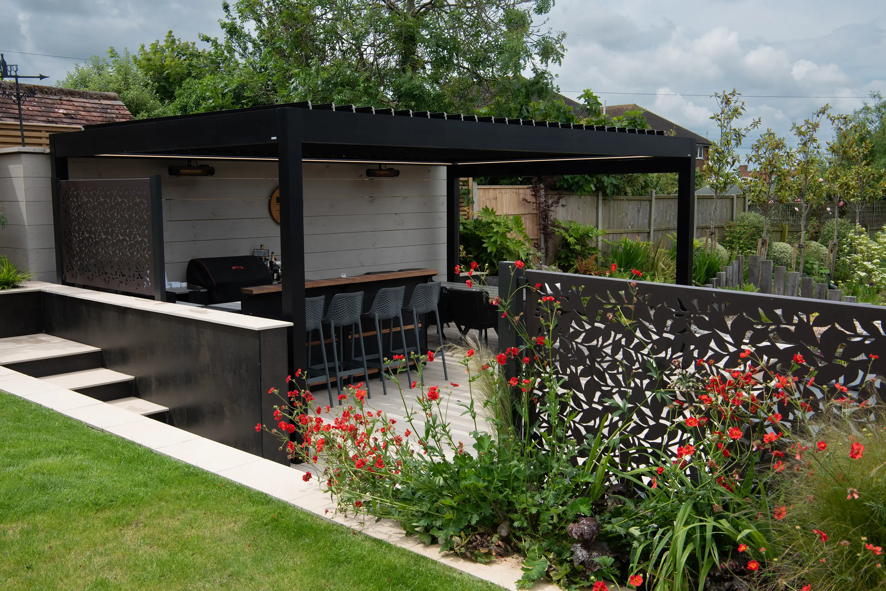 Modern outdoor structure with a shaded patio, surrounded by greenery and colorful flowers.