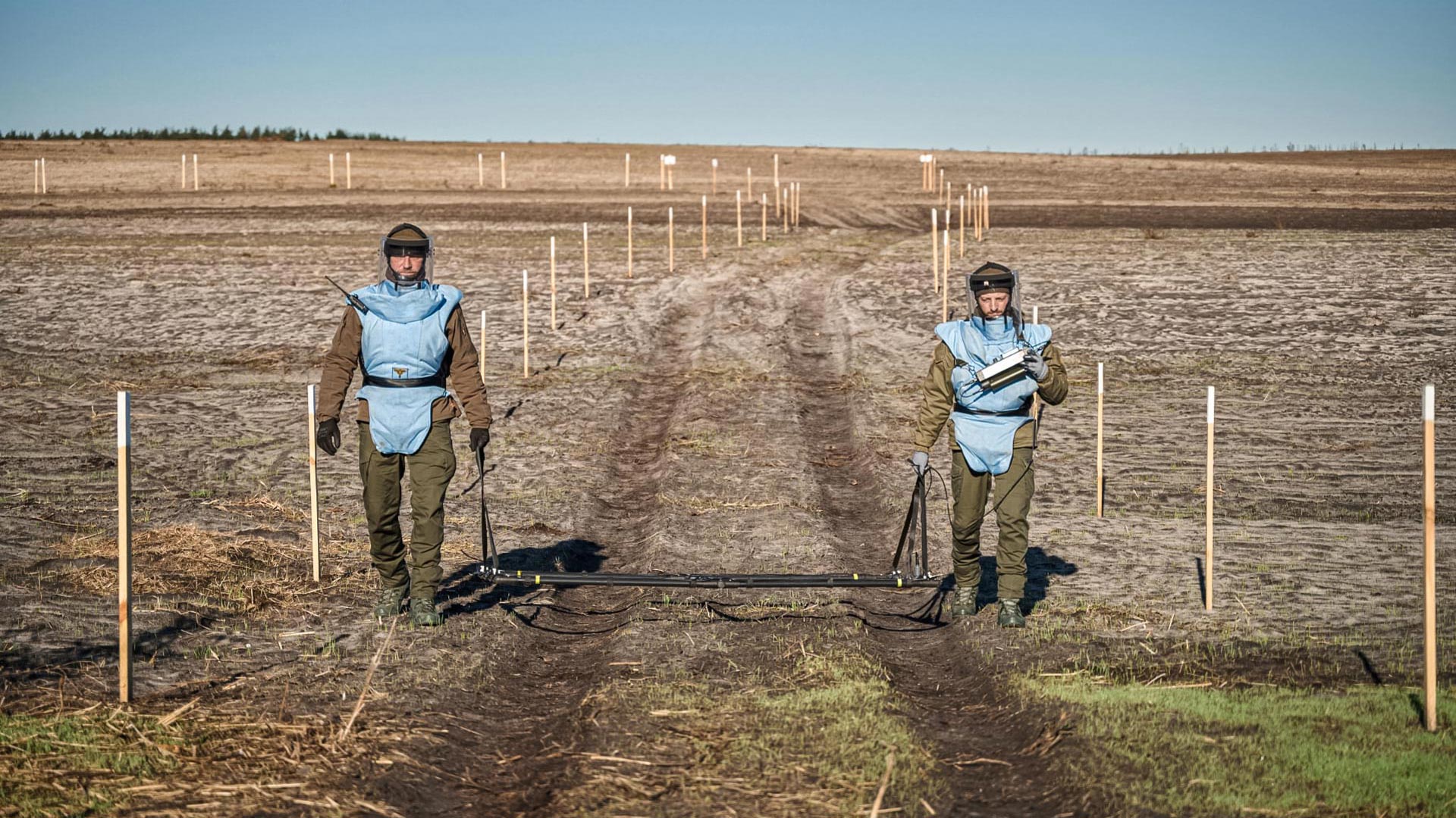 Two GCS demining operators in protective gear using a large loop detector during mine clearance operations in Irpin, Ukraine.