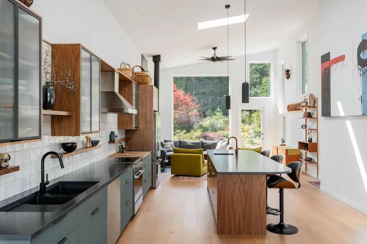 Modern two-story home with large glass windows, warmly lit interiors, and a balcony. Surrounded by trees and a manicured lawn at dusk. Cozy ambiance.