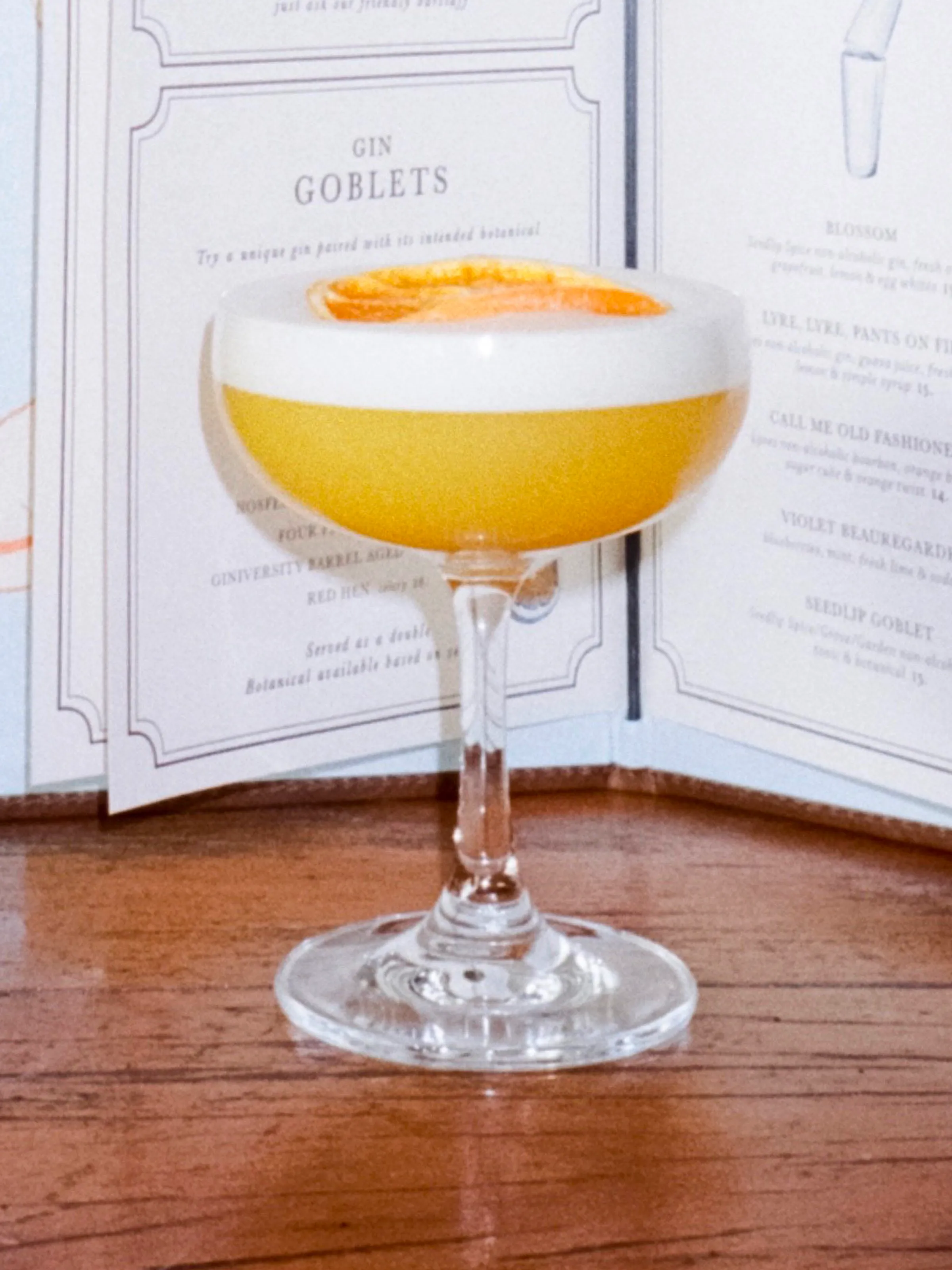 A frothy orange cocktail photographed against the open Small Bar cocktail menu