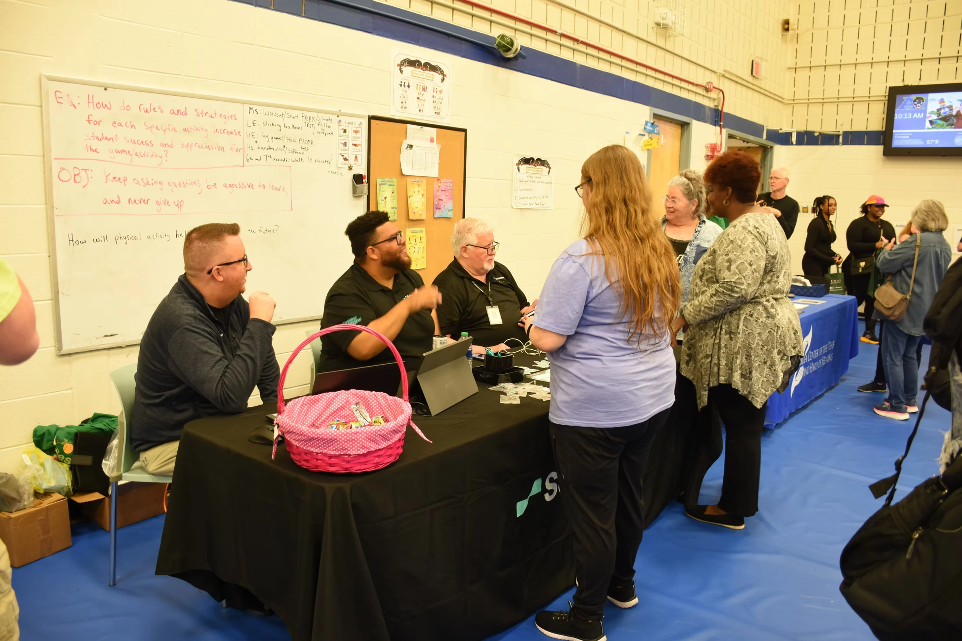People at a table at a community event. A pink basket sits on the table.