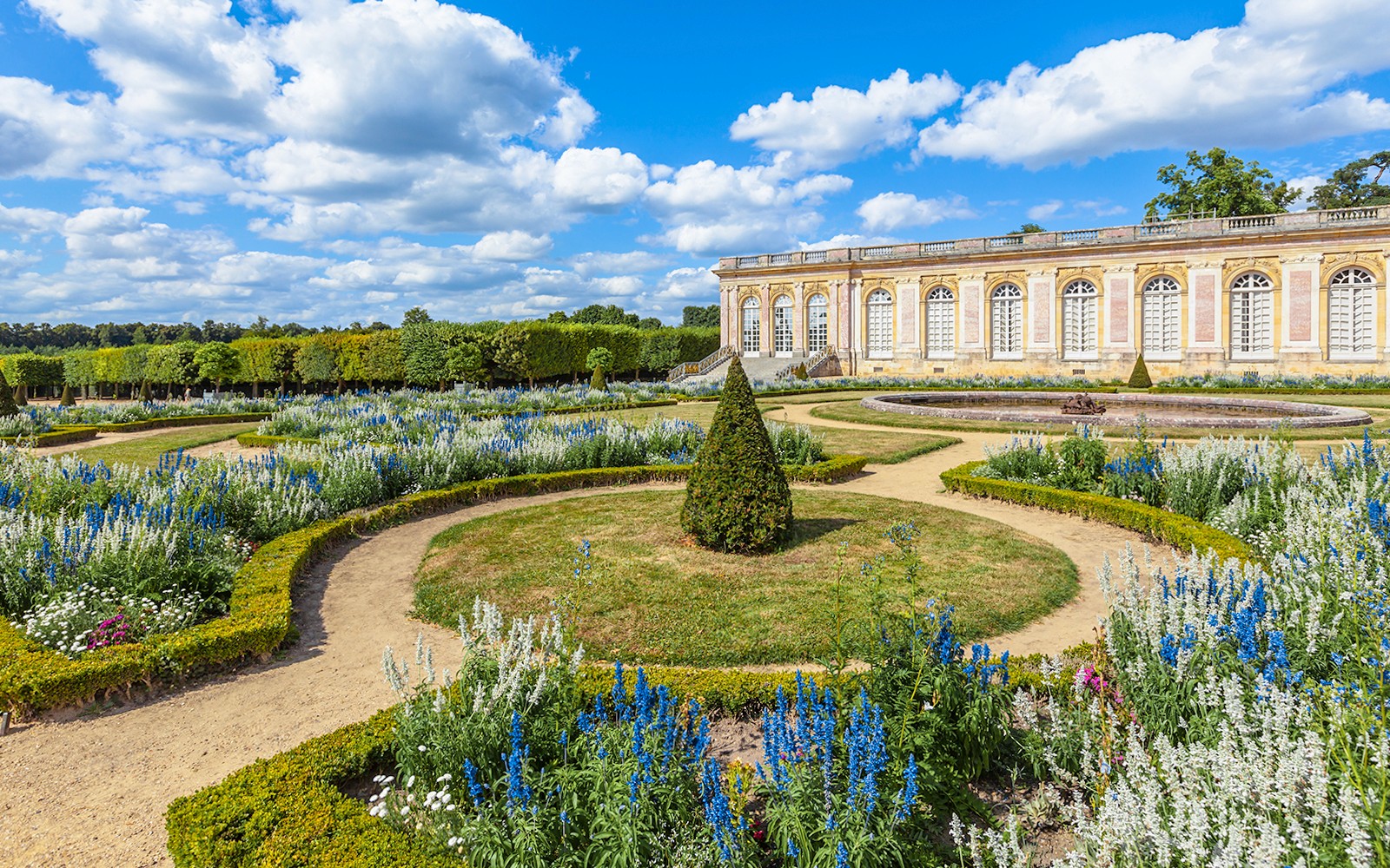 Taman Istana Grand Trianon dengan halaman rumput rapi dan hamparan bunga berwarna-warni di Versailles, Prancis.