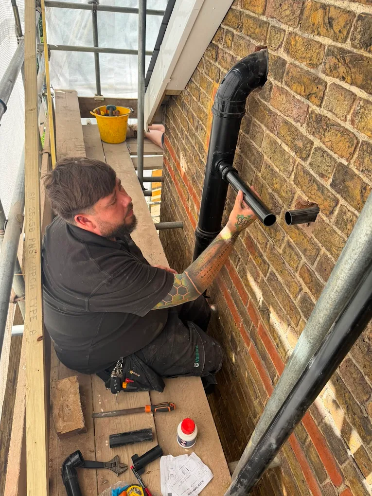Engineer fitting a black soil pipe from scaffolding.