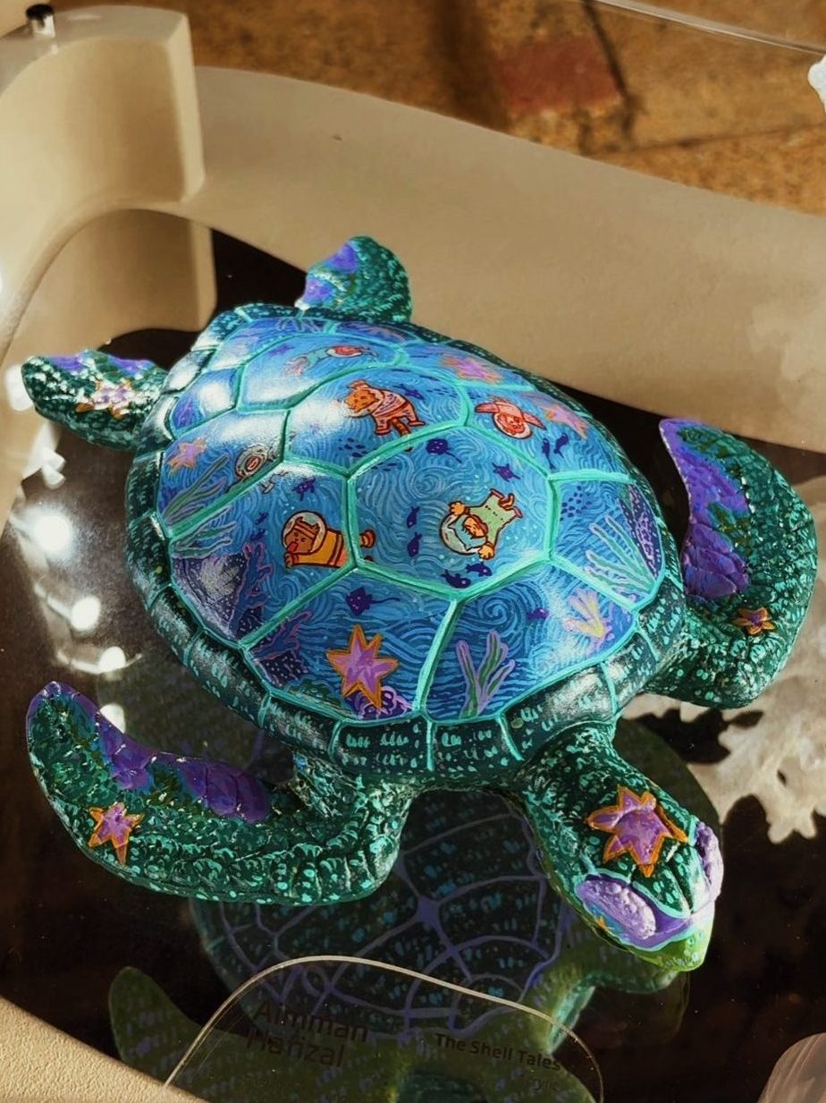 A handmade turtle sculpture featuring vibrant colors and intricate designs, including marine life details, displayed in a protective case.