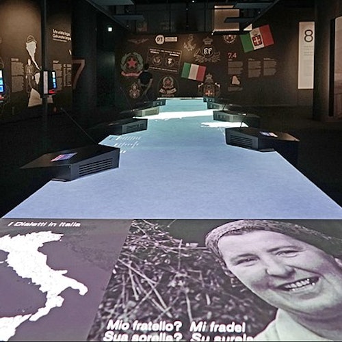 Mostra interattiva con immagini storiche, una mappa dell’Italia e testi in italiano. Sono presenti esposizioni di bandiere e schermi di proiezione.