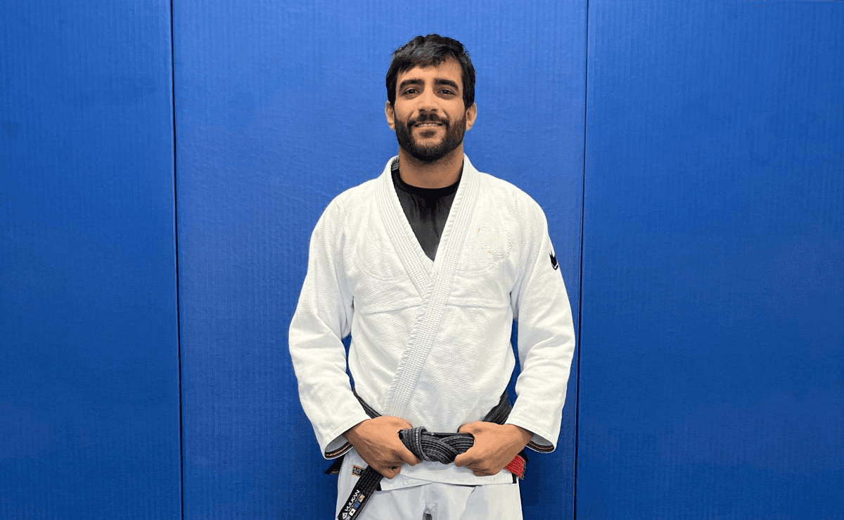Maria Elisa Thimoteo smiling in a white gi, arms folded, in front of a gradient backdrop