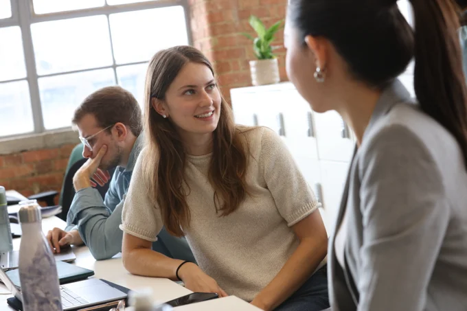 Colleagues talking and collaborating at desks in a contemporary open-plan office environment.