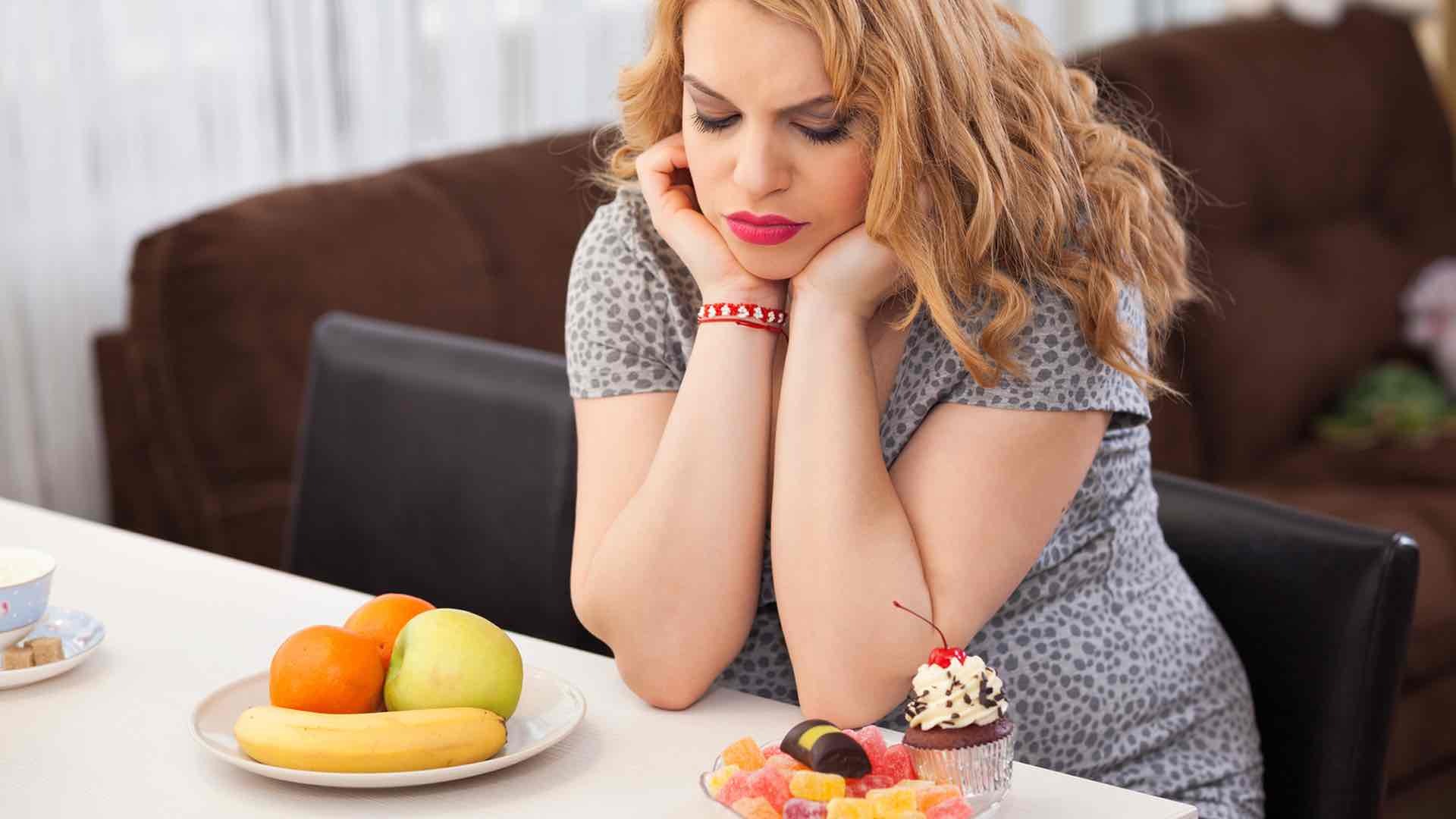 woman contemplating between eating fruits or carb-loaded snacks