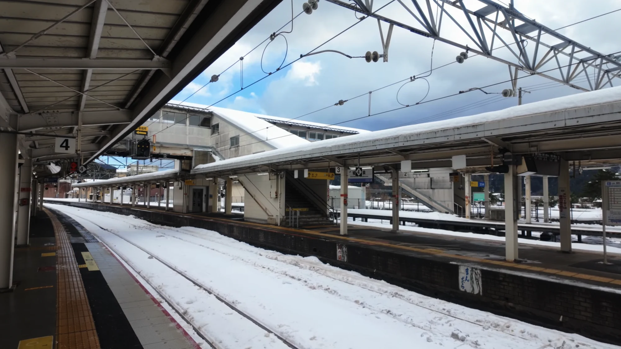 A snow-covered platform at Kinosaki Onsen station with the track running away under grey sky.