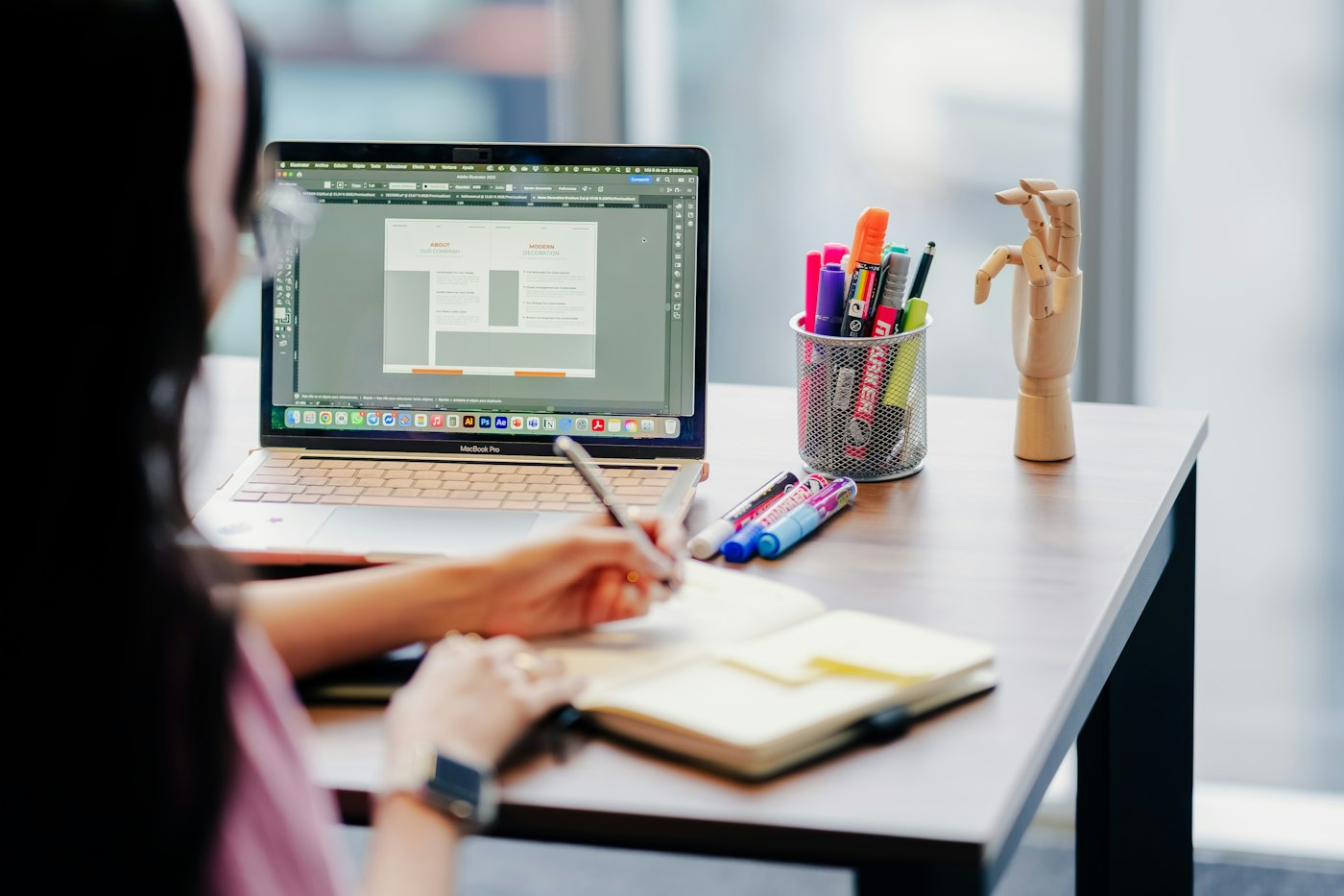 Designer sketching layouts in a notebook beside a laptop