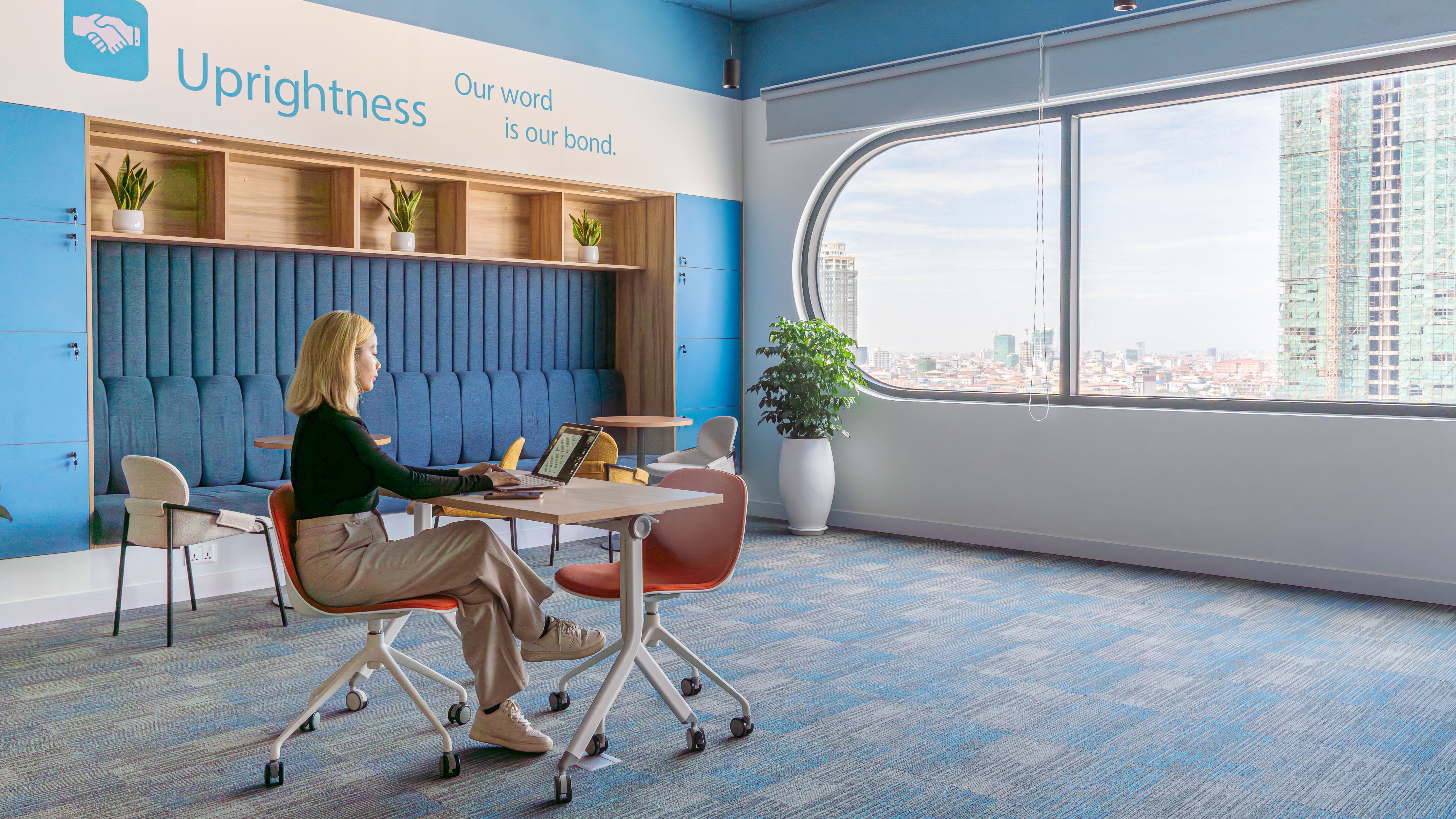 Open collaboration zone featuring branded wall graphics, shared tables, and soft seating aligned with workplace booking systems and flexible use
