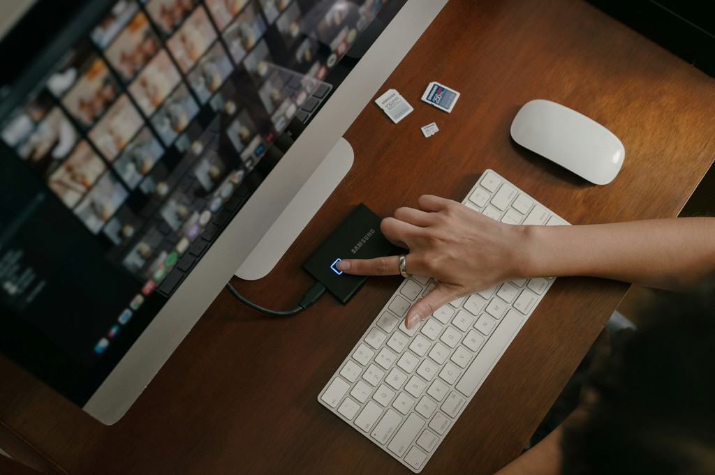 A person organizes digital photos on a computer, transferring files using a Samsung external drive and SD cards, illustrating data management and photo editing workflow.